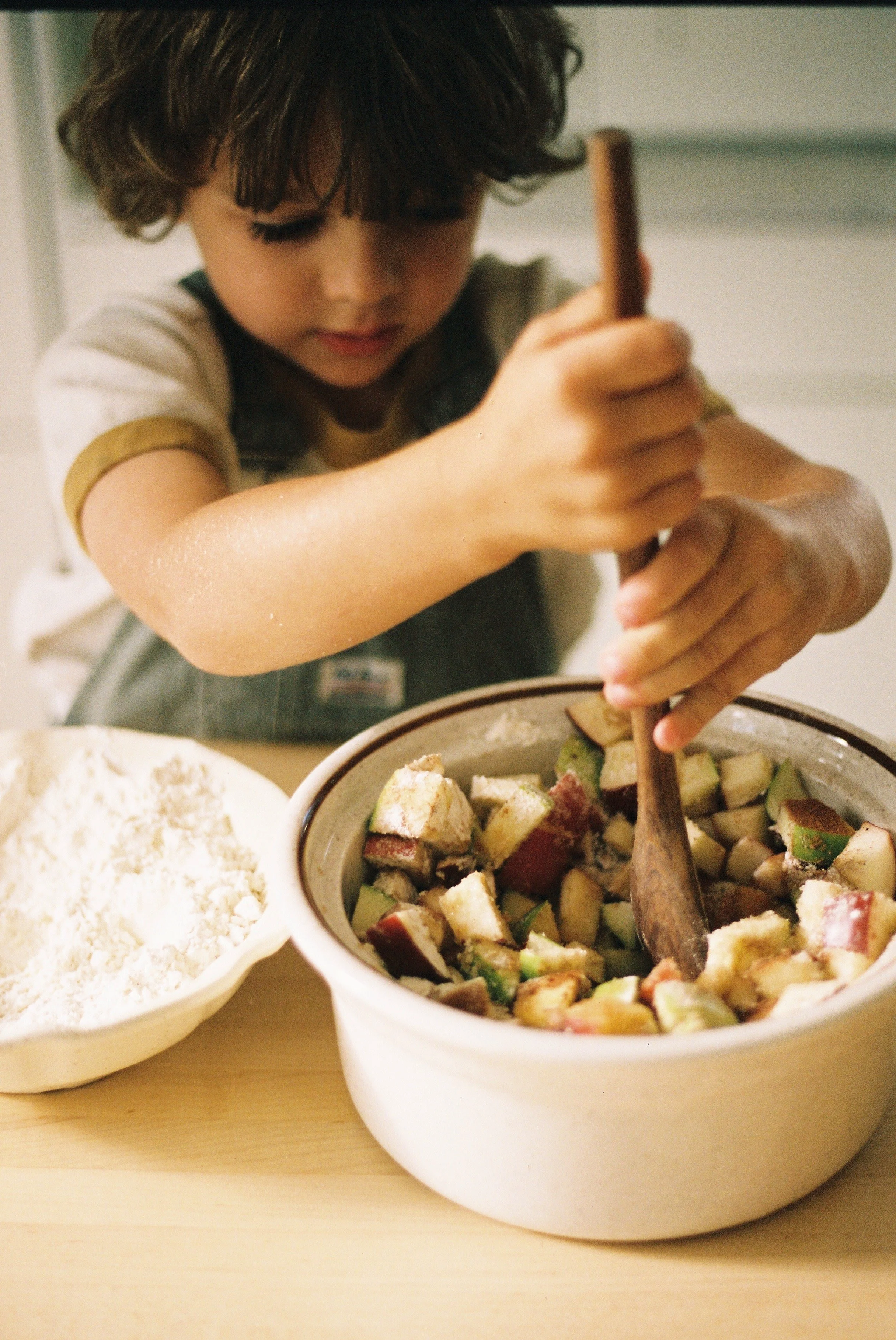 A boy stirring a crock full of apples.