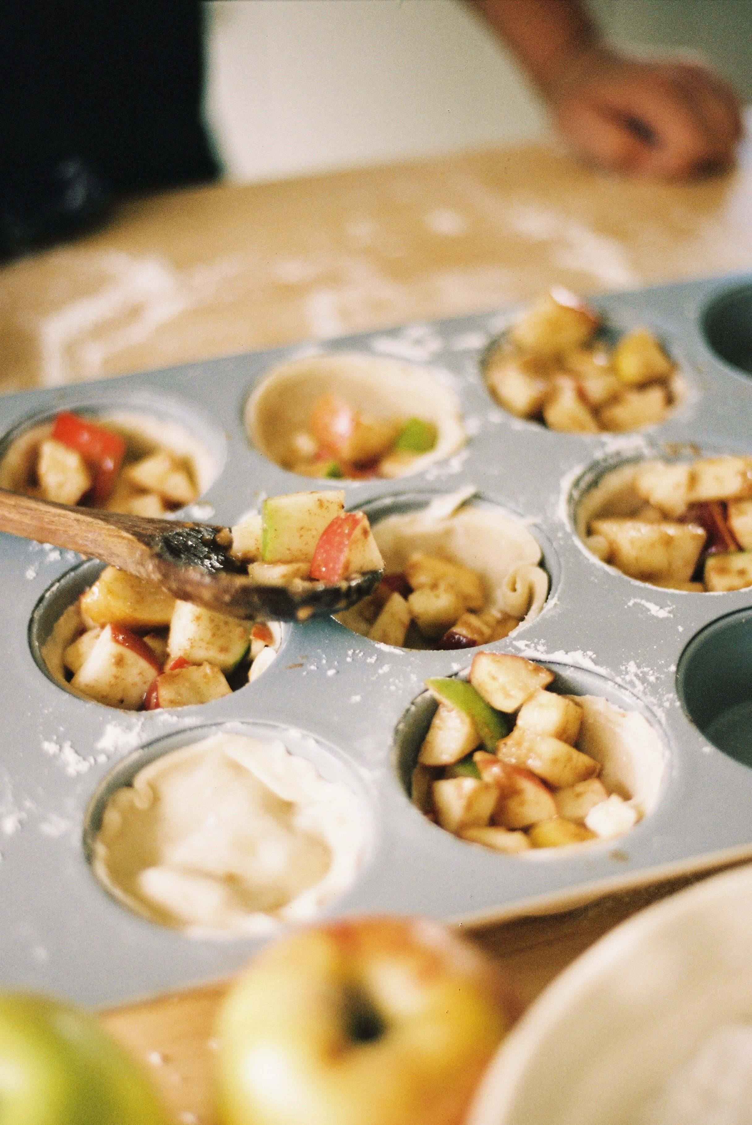 A wooden spoon scooping apple filling into a cupcake mold.