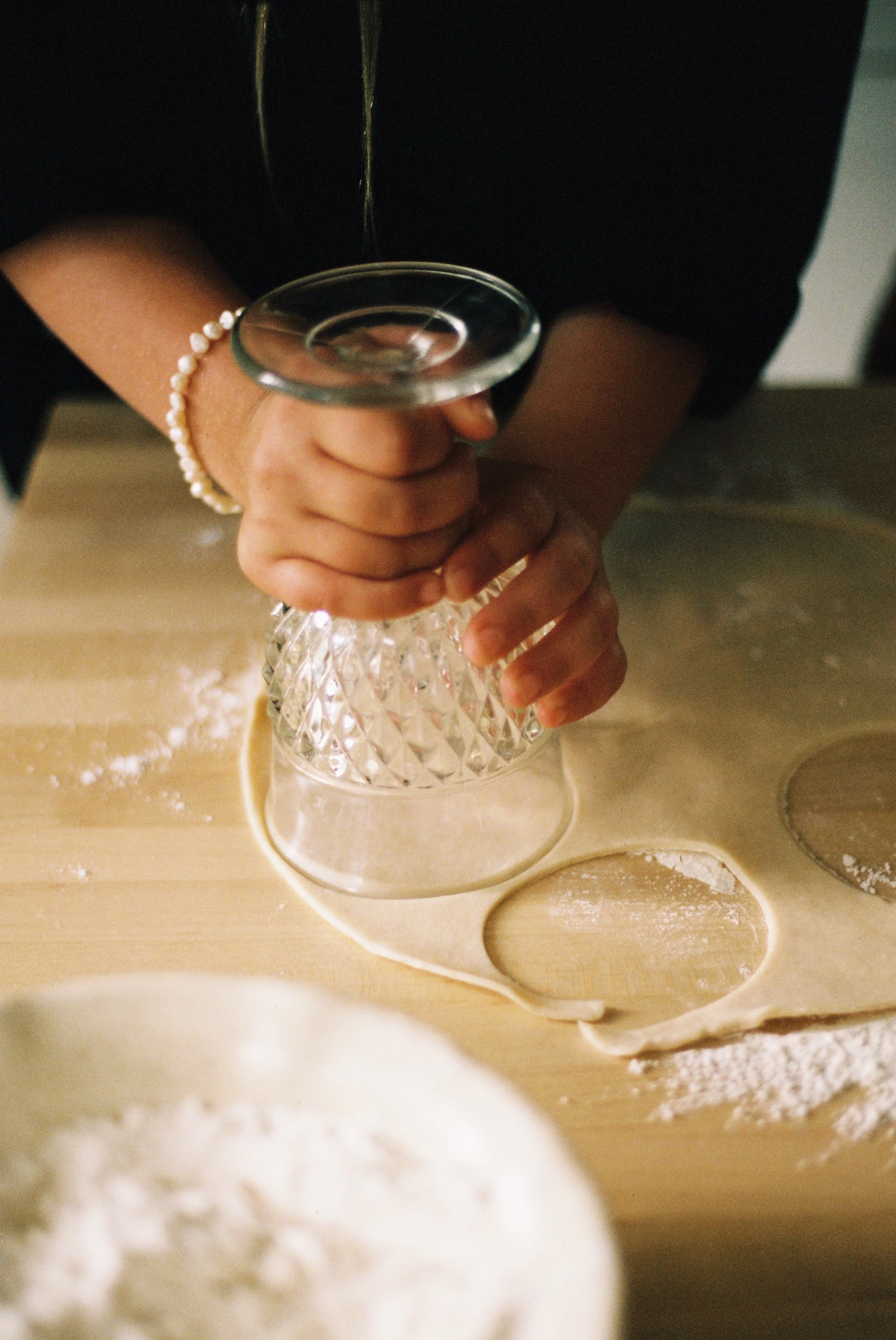 Closeup of a child using a glass cup to cut circles in dough.