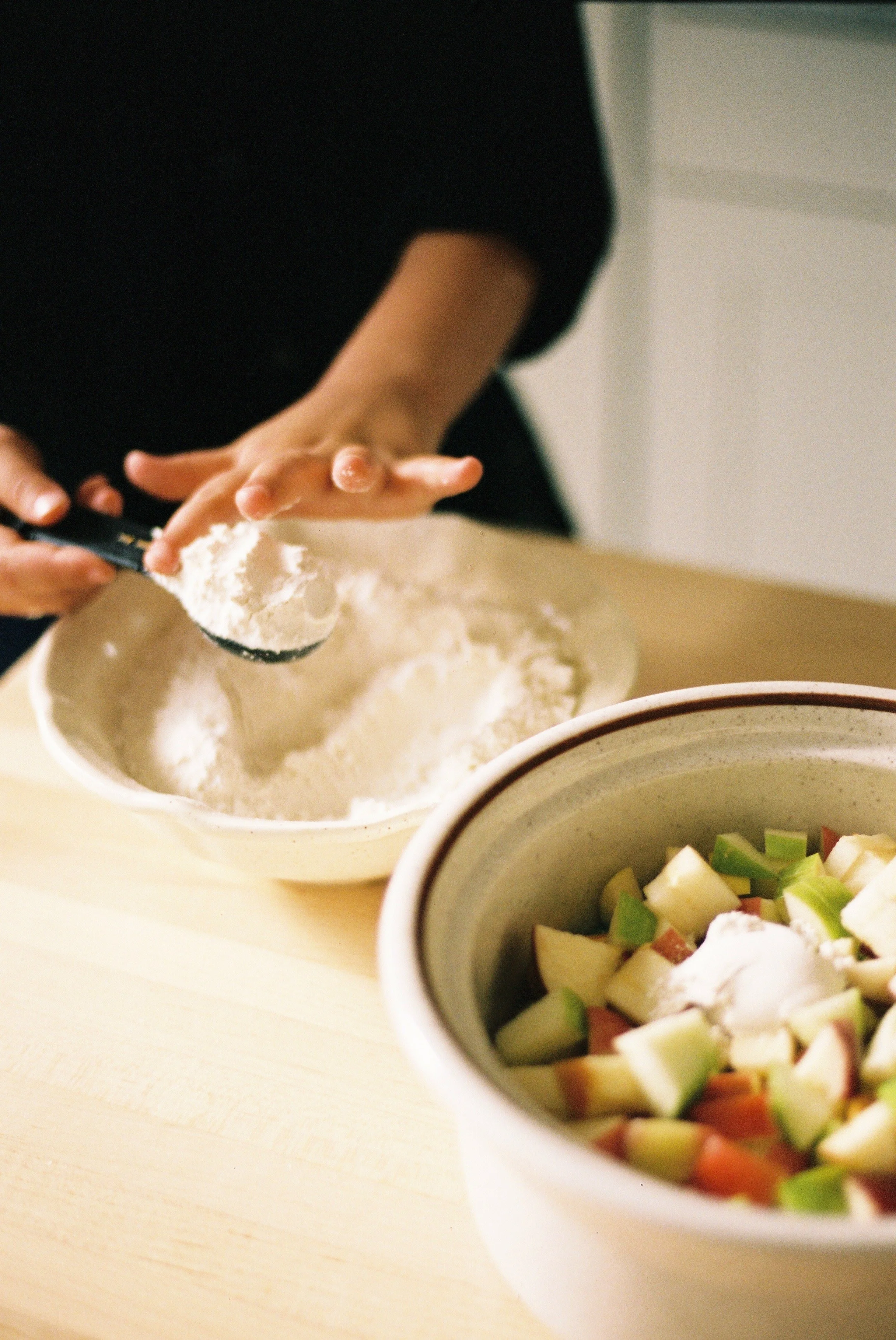 A child scooping flour from a bowl.