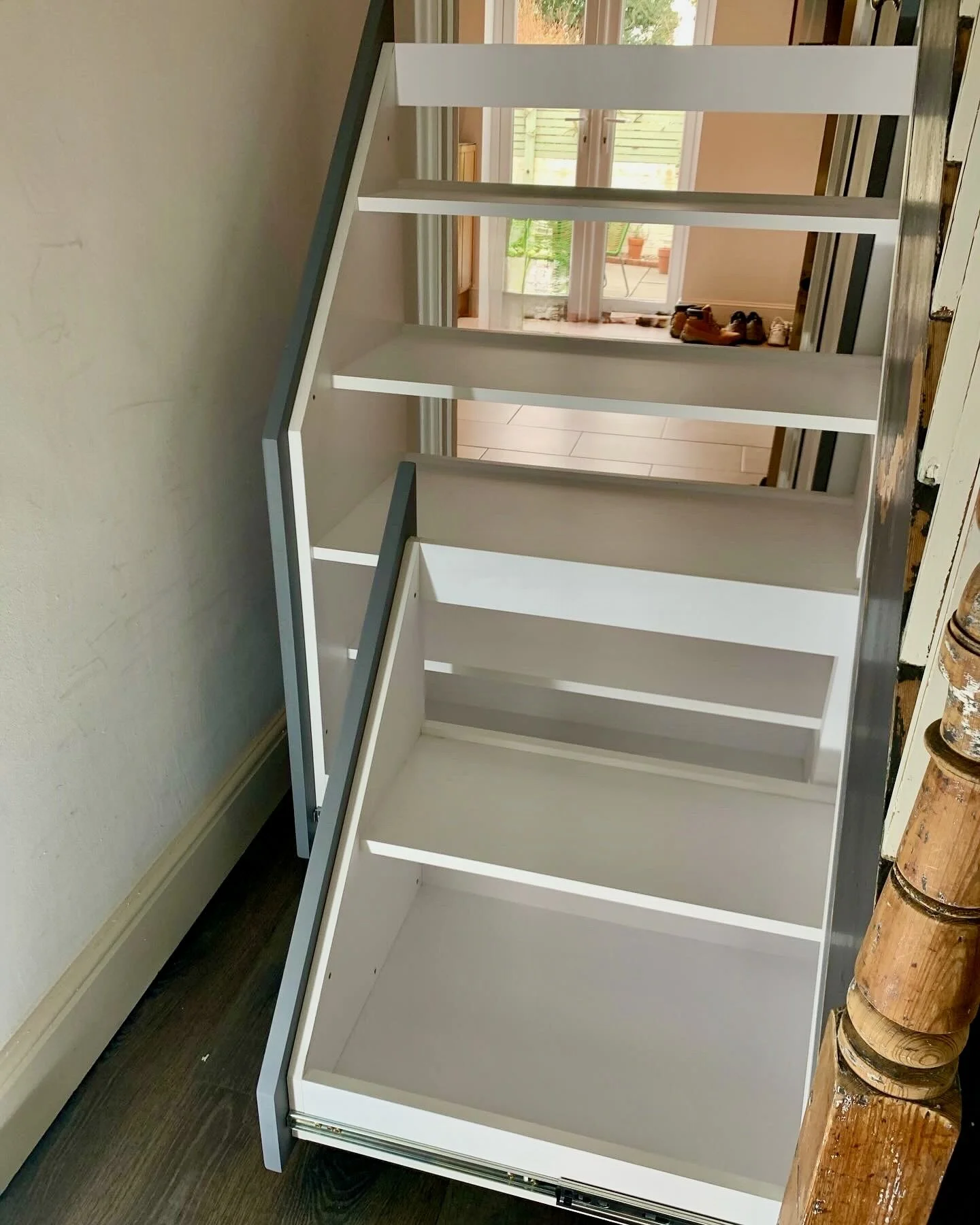 White wooden cabinet with open drawers and shelves, placed near a staircase and a wall.