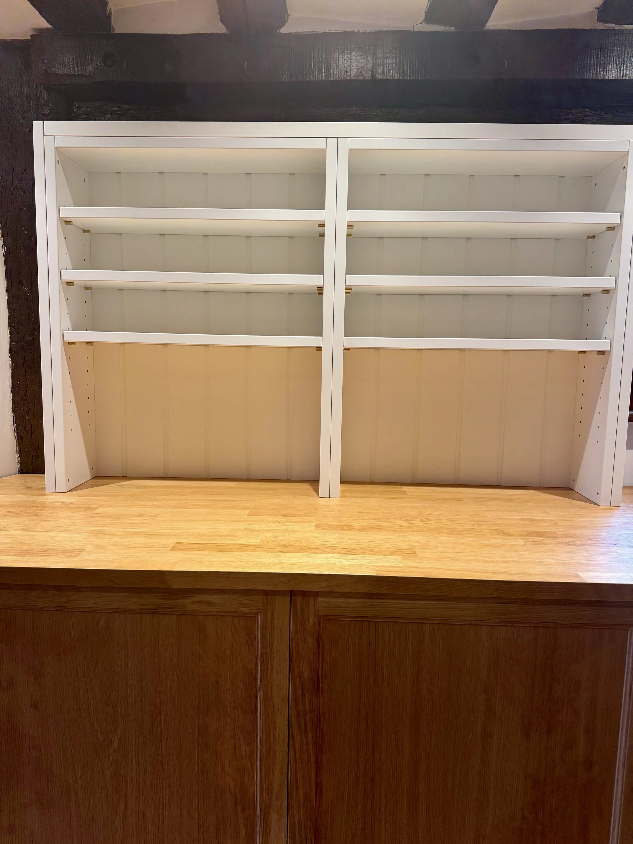 Empty white shelving unit on a wooden countertop against a wall with wood paneling.