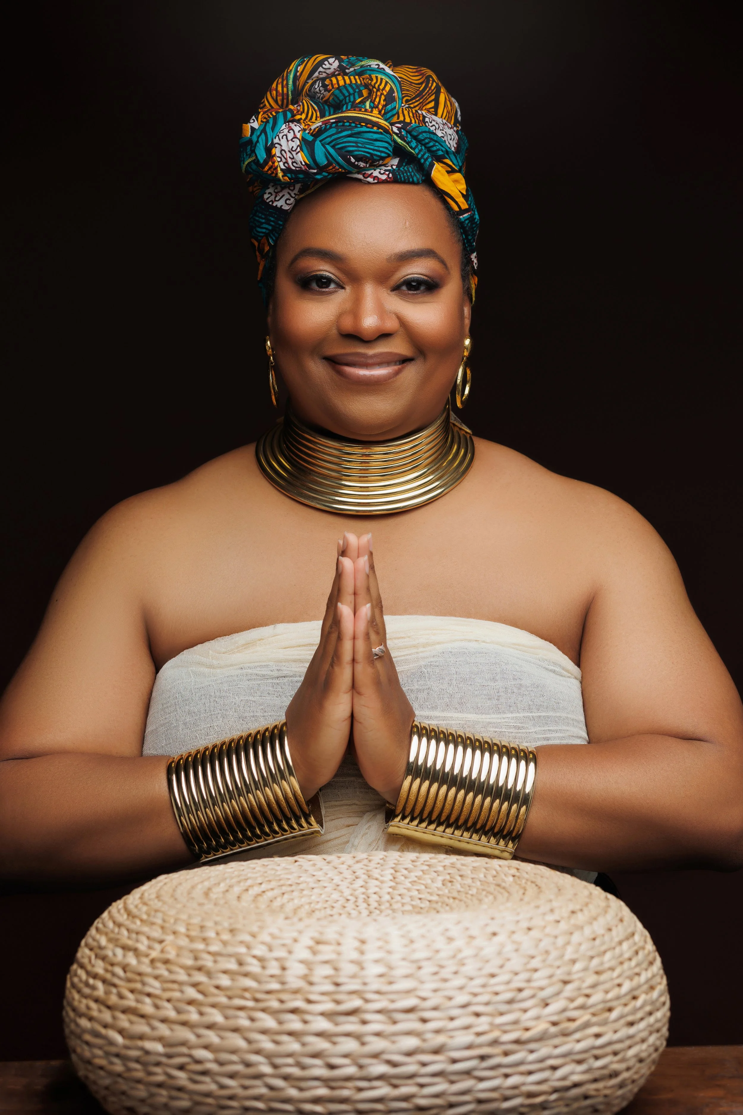 Legacy portrait of a confident woman wearing a headwrap and gold jewelry with hands in prayer, photographed in a Memphis Tennessee studio by Hadonica’s Photography.