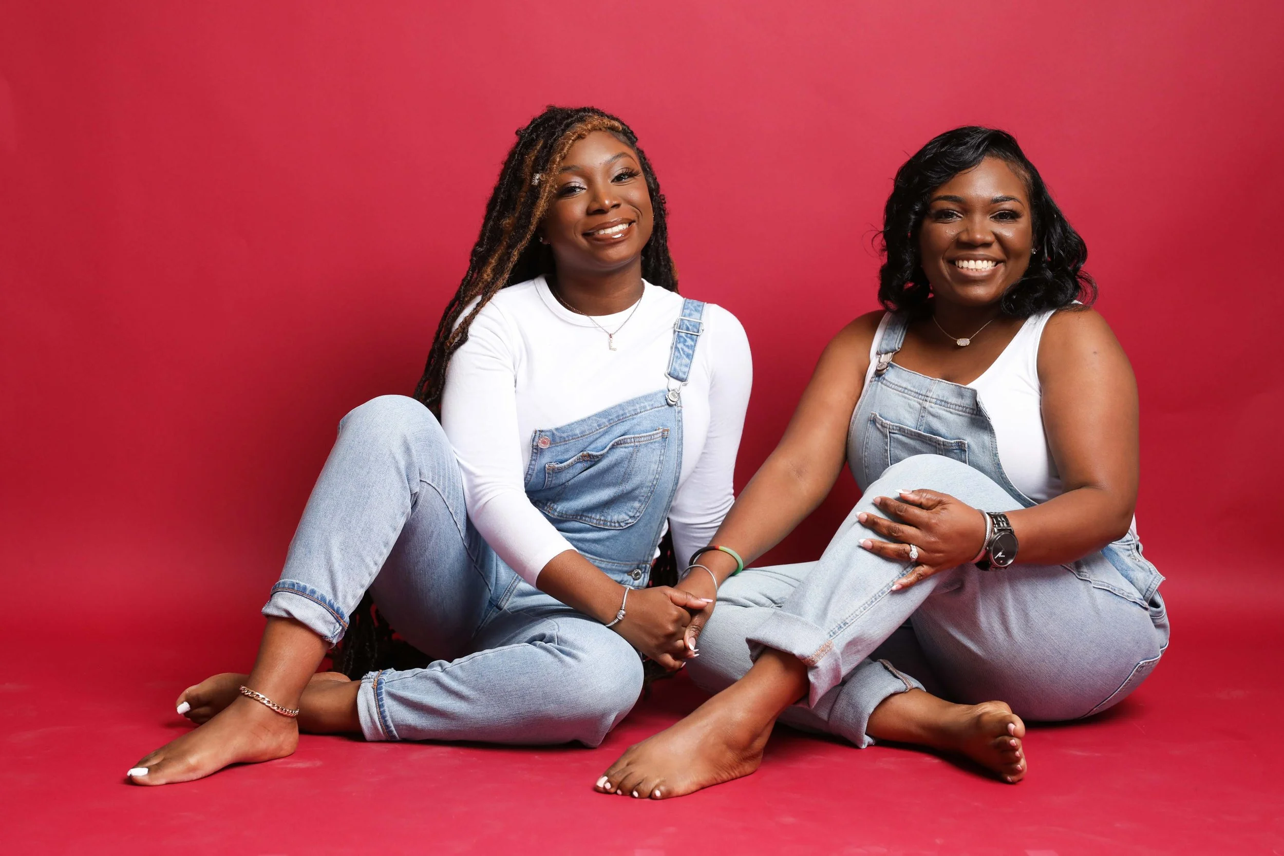 Mother and high school senior daughter sitting together smiling at camera in Memphis studio photoshoot with red backdrop