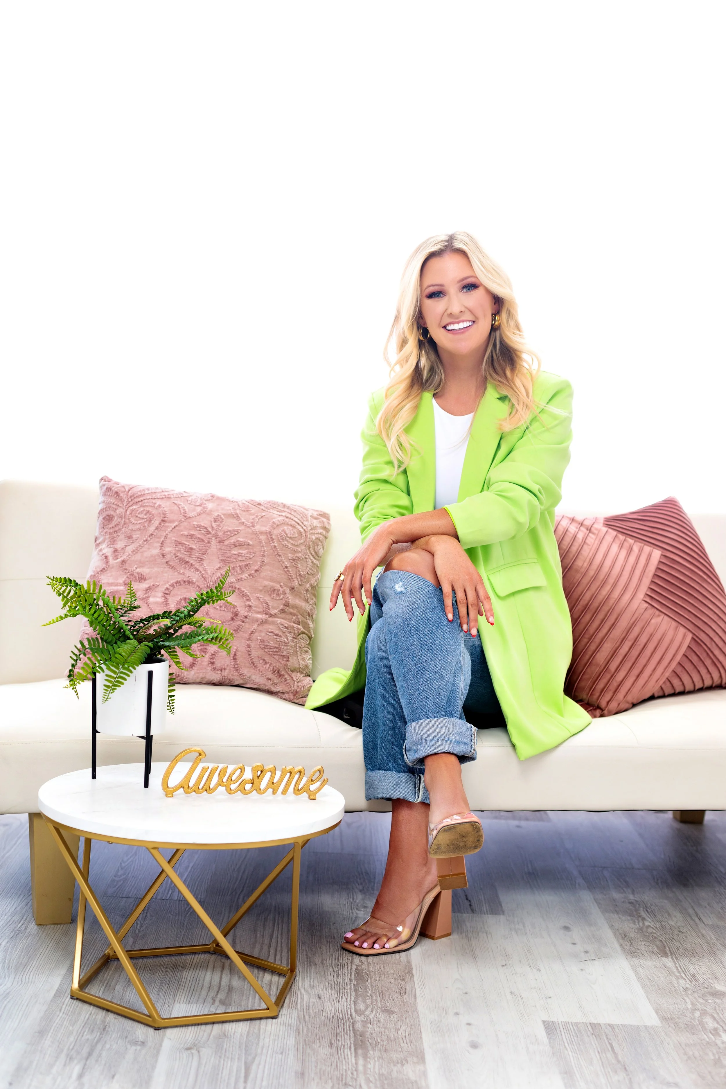 Professional branding portrait of a smiling entrepreneur wearing a green blazer sitting on a couch in a Memphis photography studio