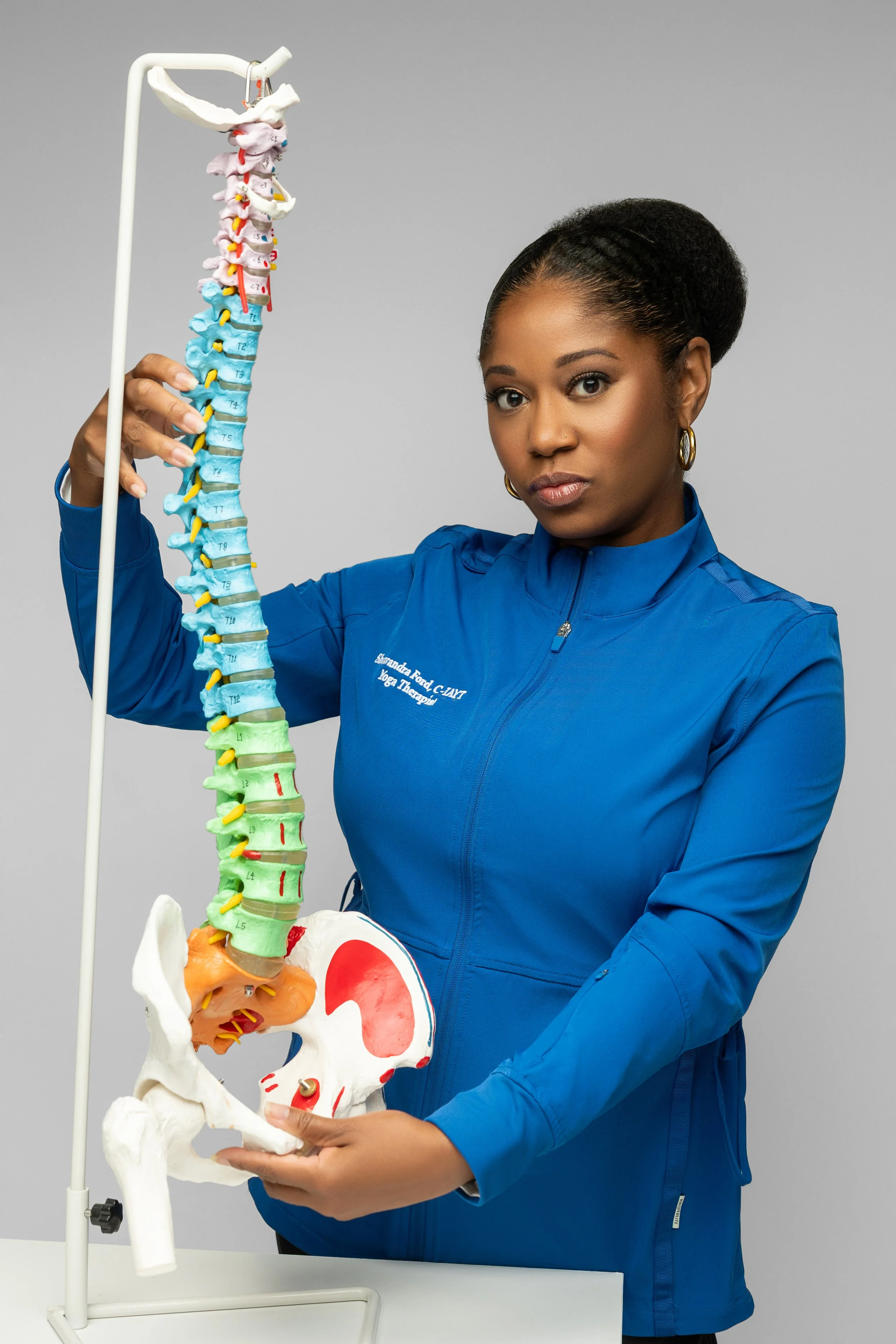 A woman in a blue jacket holding a model of a human spine and pelvis.
