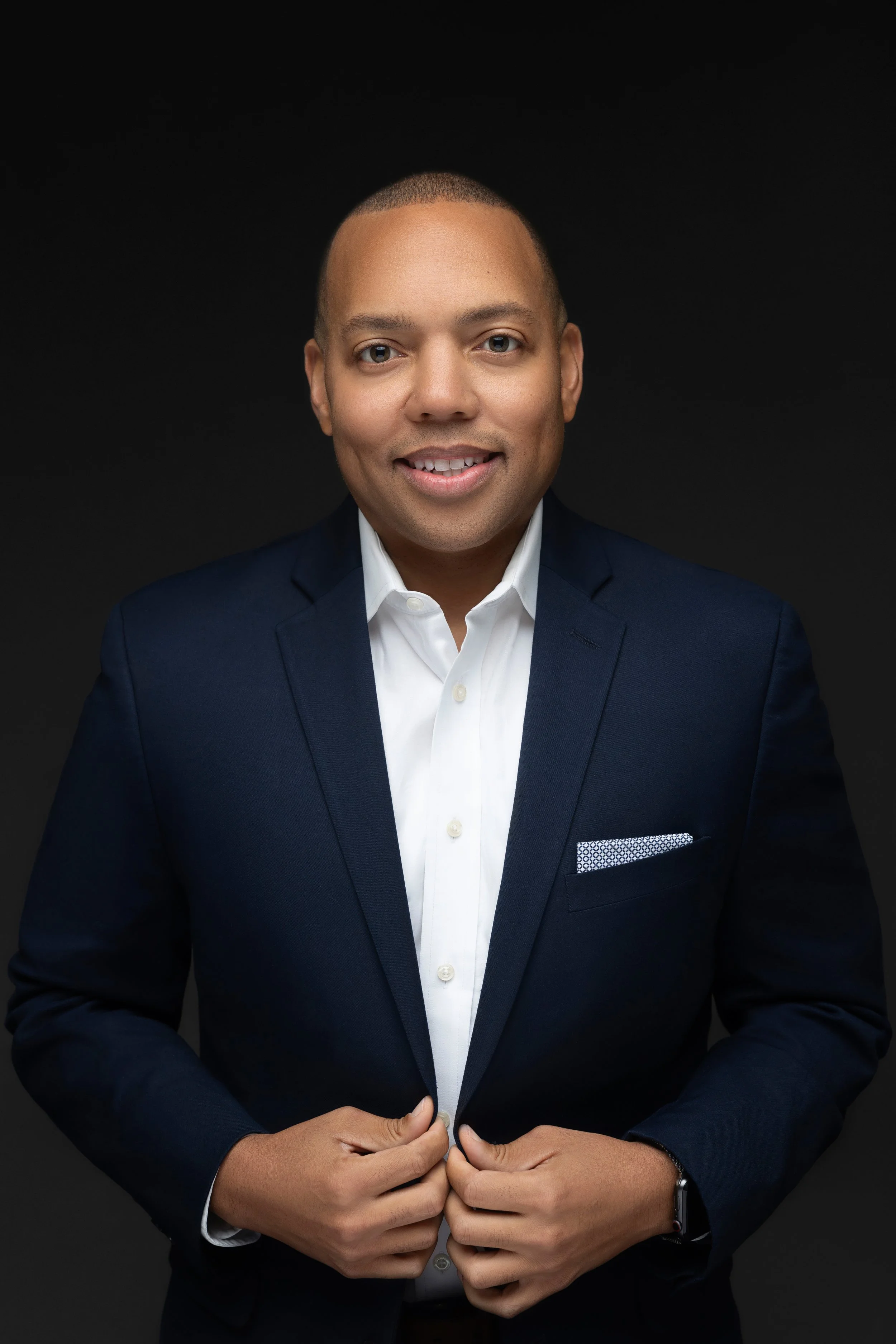Professional studio headshot of a confident man in a navy suit against a dark backdrop, Hadonica's Photography in Memphis tennessee, professional headshots in memphis tn