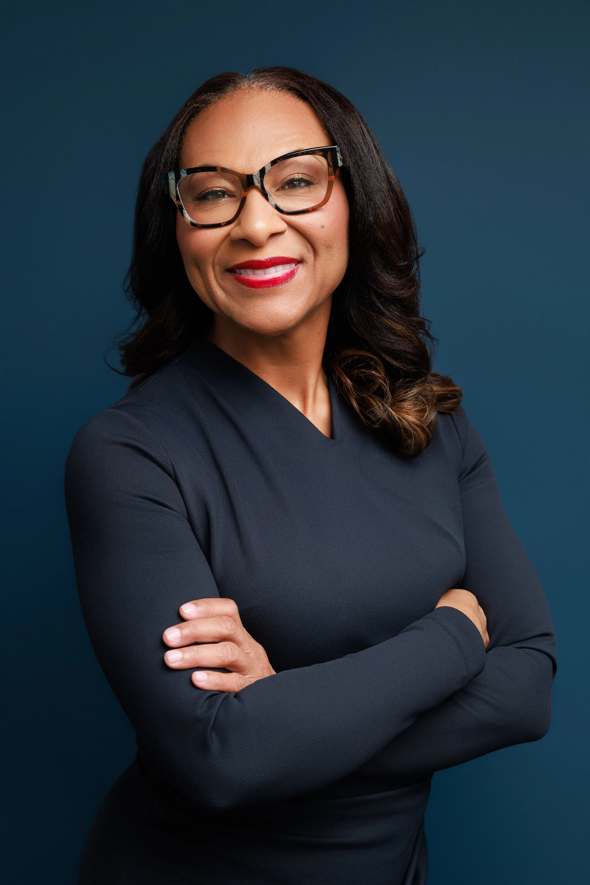 Professional headshot of university professor with arms crossed wearing dark dress on blue background Memphis studio