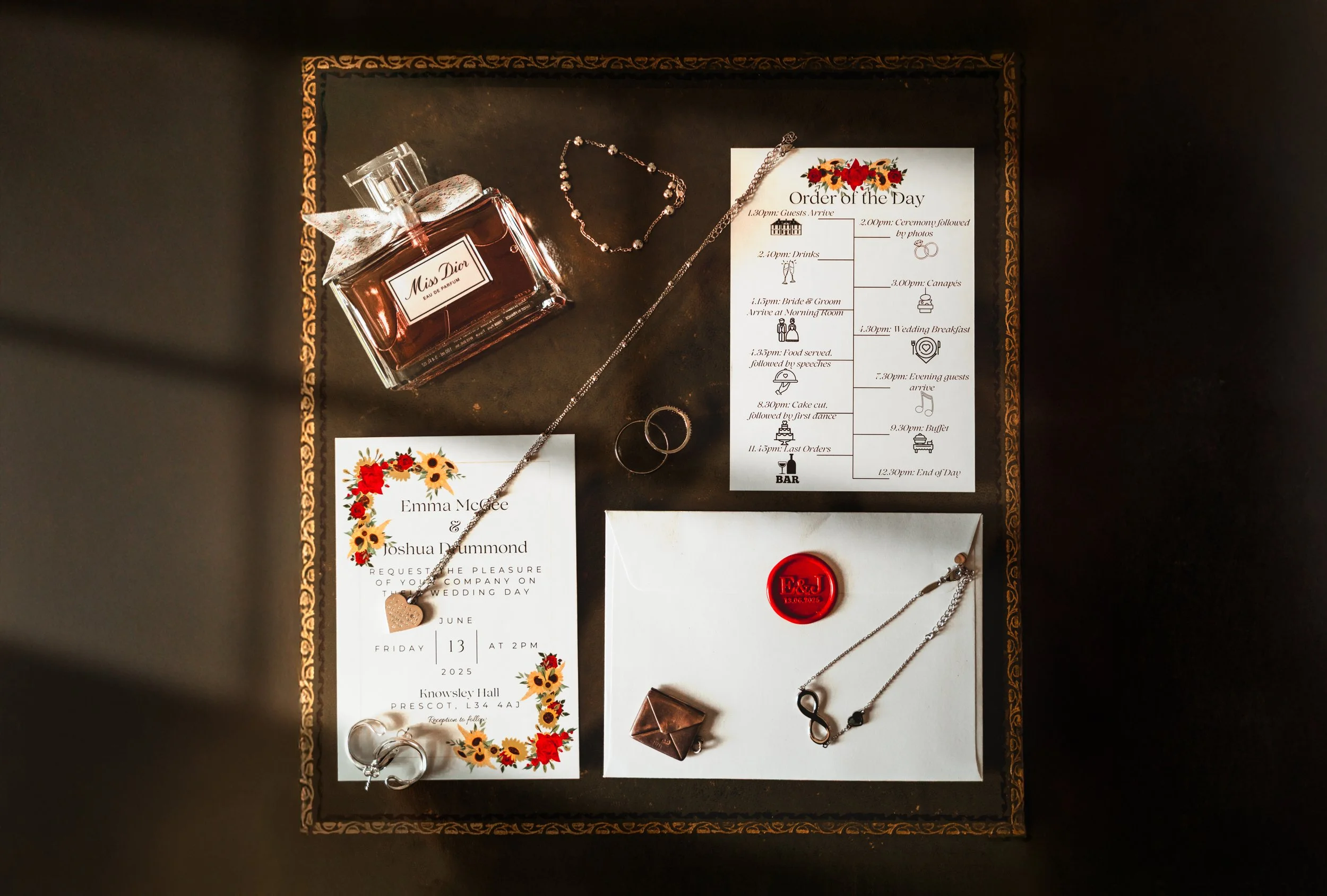 Wedding invitation suite with floral designs, jewelry including necklaces and rings, perfume bottle, and decorative seals on a tray.