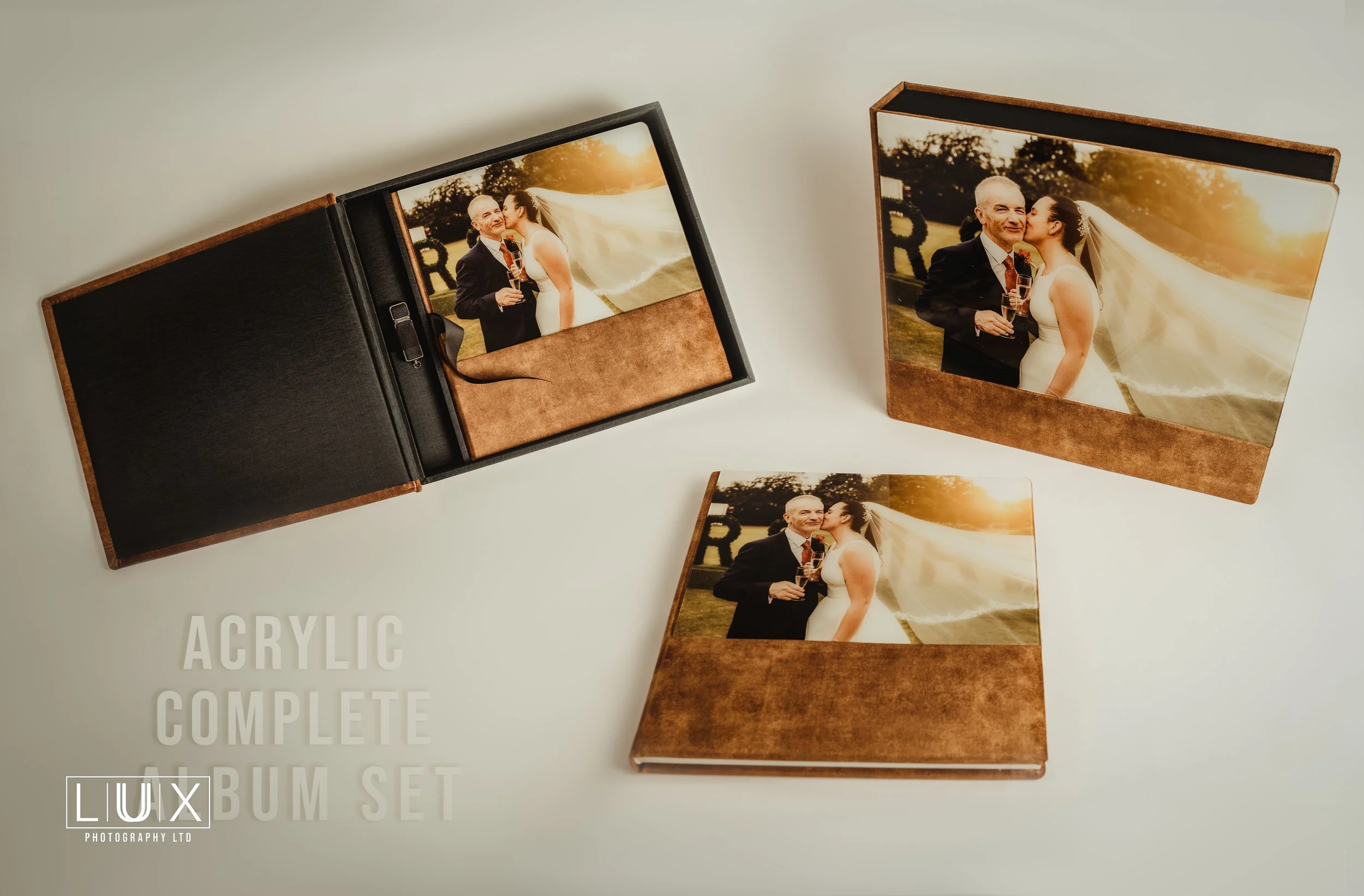 A complete acrylic wedding photo album set shown with the album closed and open, containing a picture of a newlywed couple at sunset. The set includes a black and brown album case and a separate photo book, all displayed on a white surface.