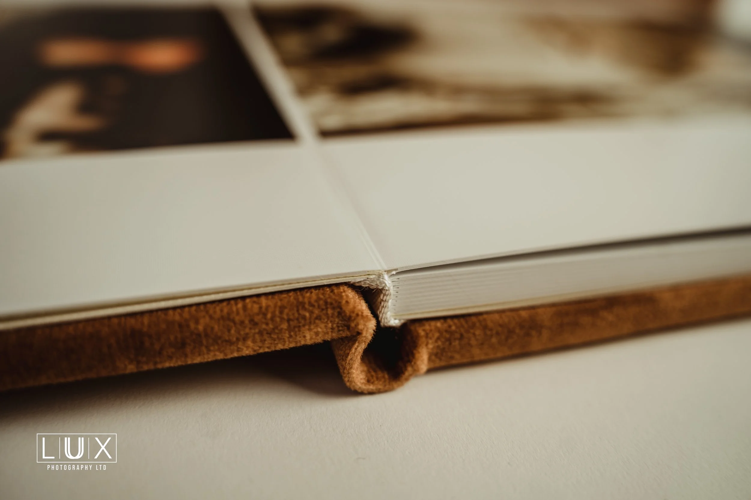Close-up of an open photo book resting on another book with a brown suede cover, on a white surface.