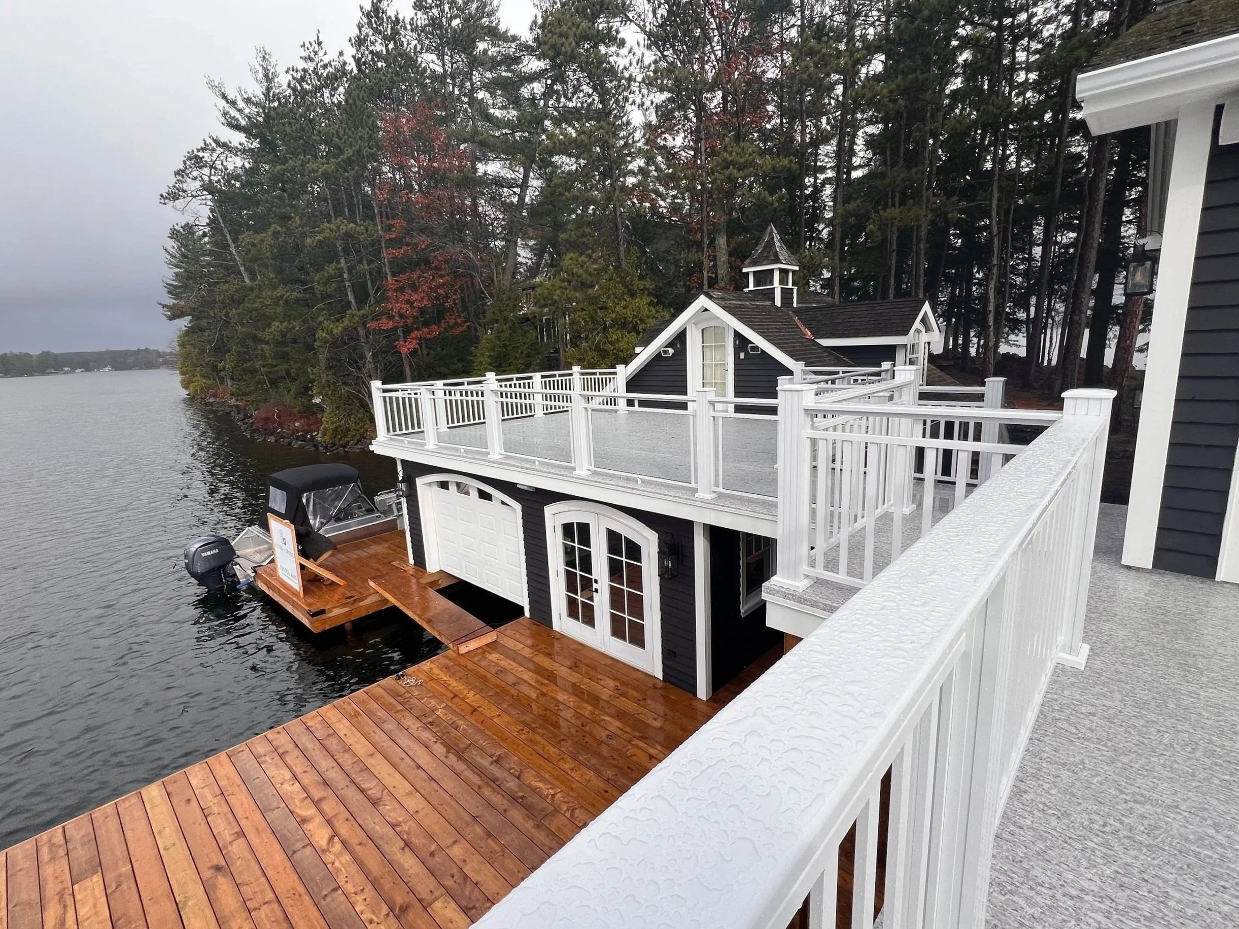 alt="White and black boathouse with cedar dock on Muskoka lake"