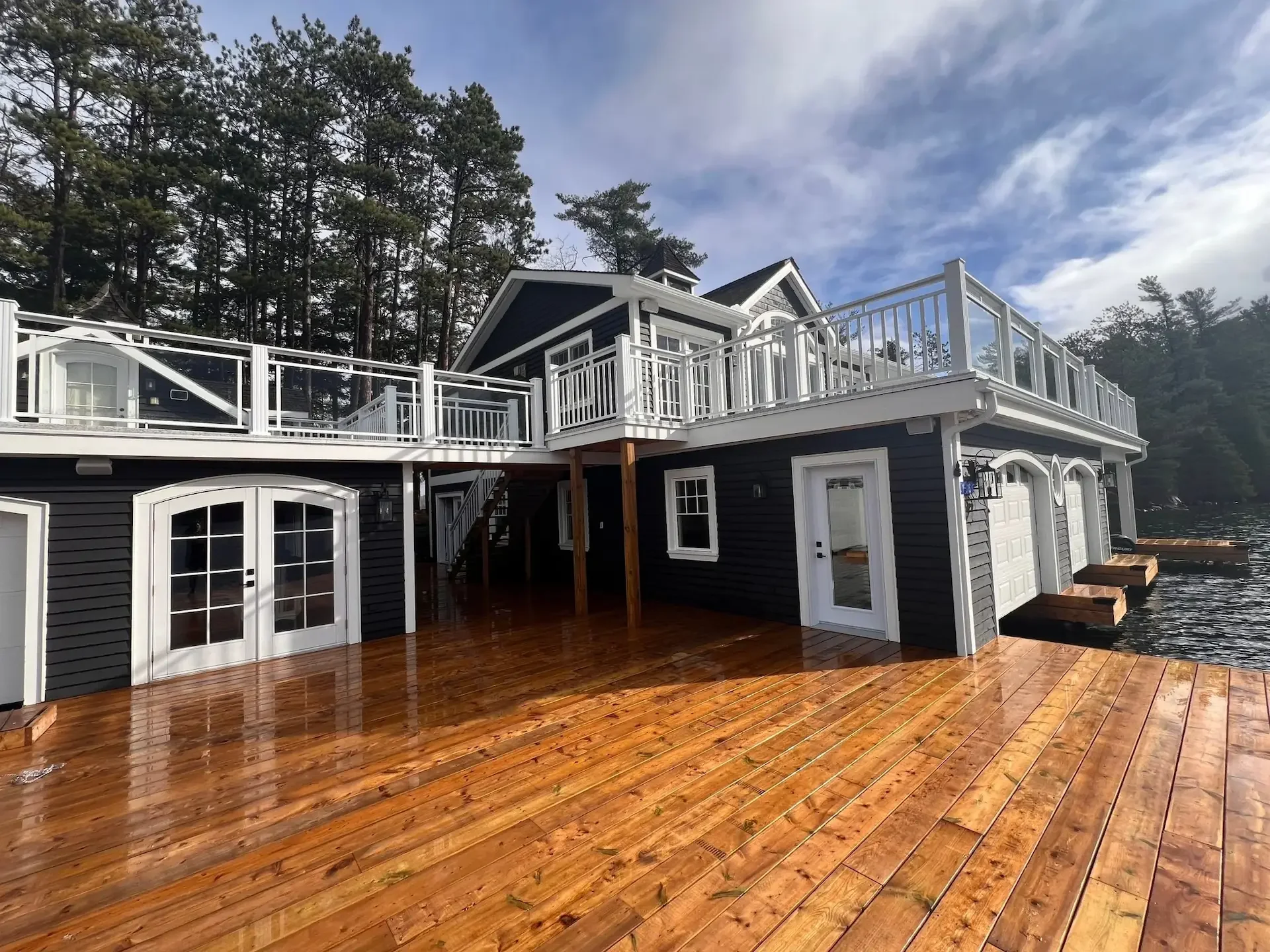 Muskoka boathouse with dark siding, white railings and a wood dock