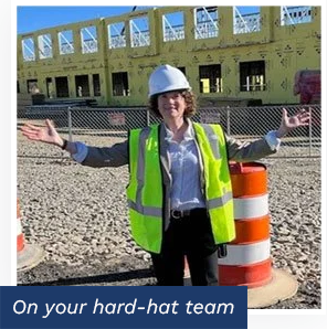 Mary Knowles at a construction site wearing a hard hat and high-visibility safety vest in front of a building under construction.