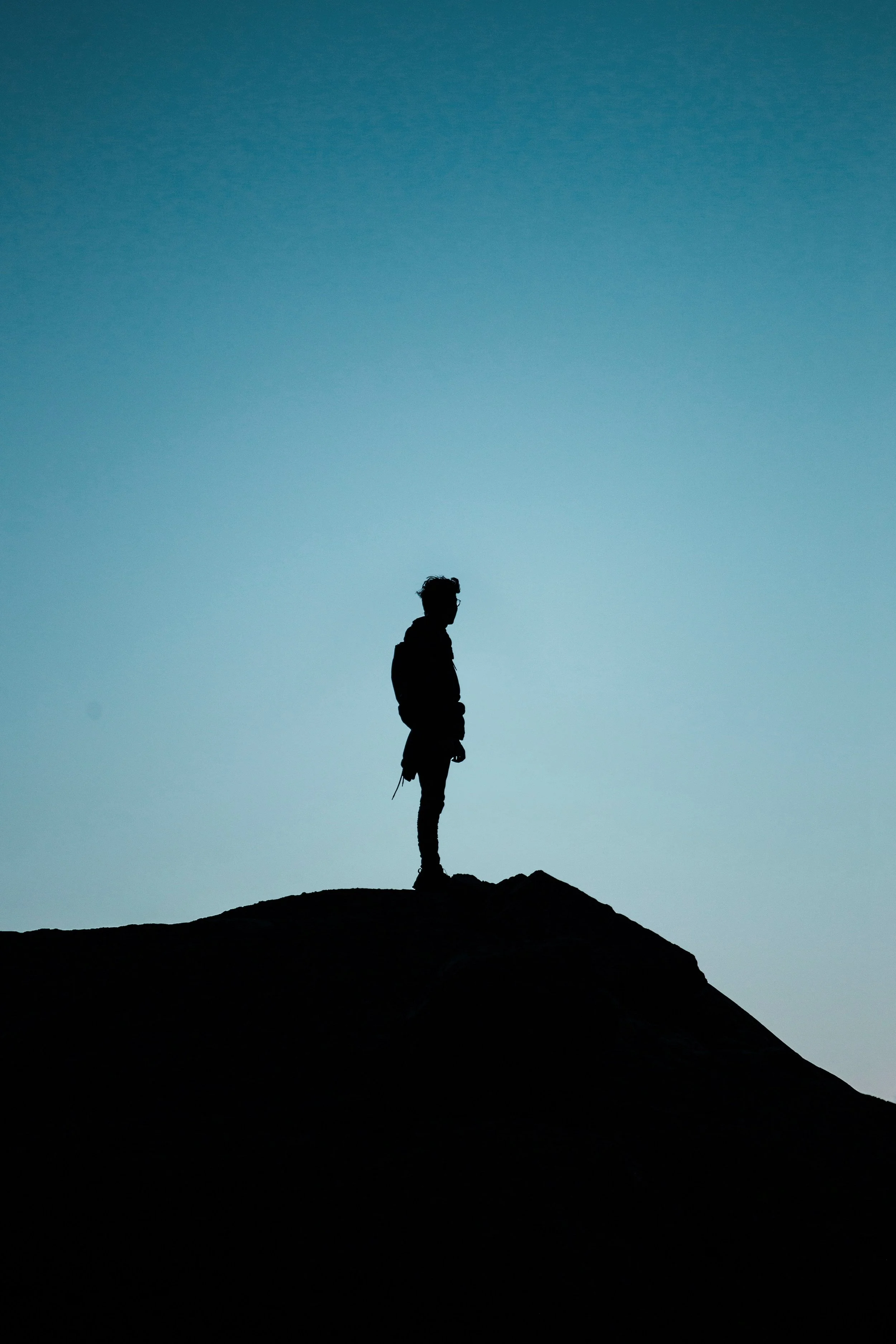 Silhouette of a person standing on a mountain peak against a gradient sky at dusk.