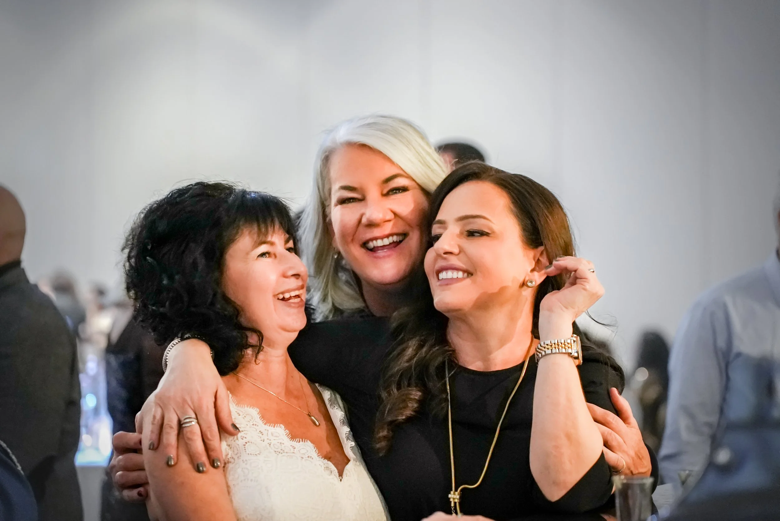 Three women smiling and hugging at a social gathering.