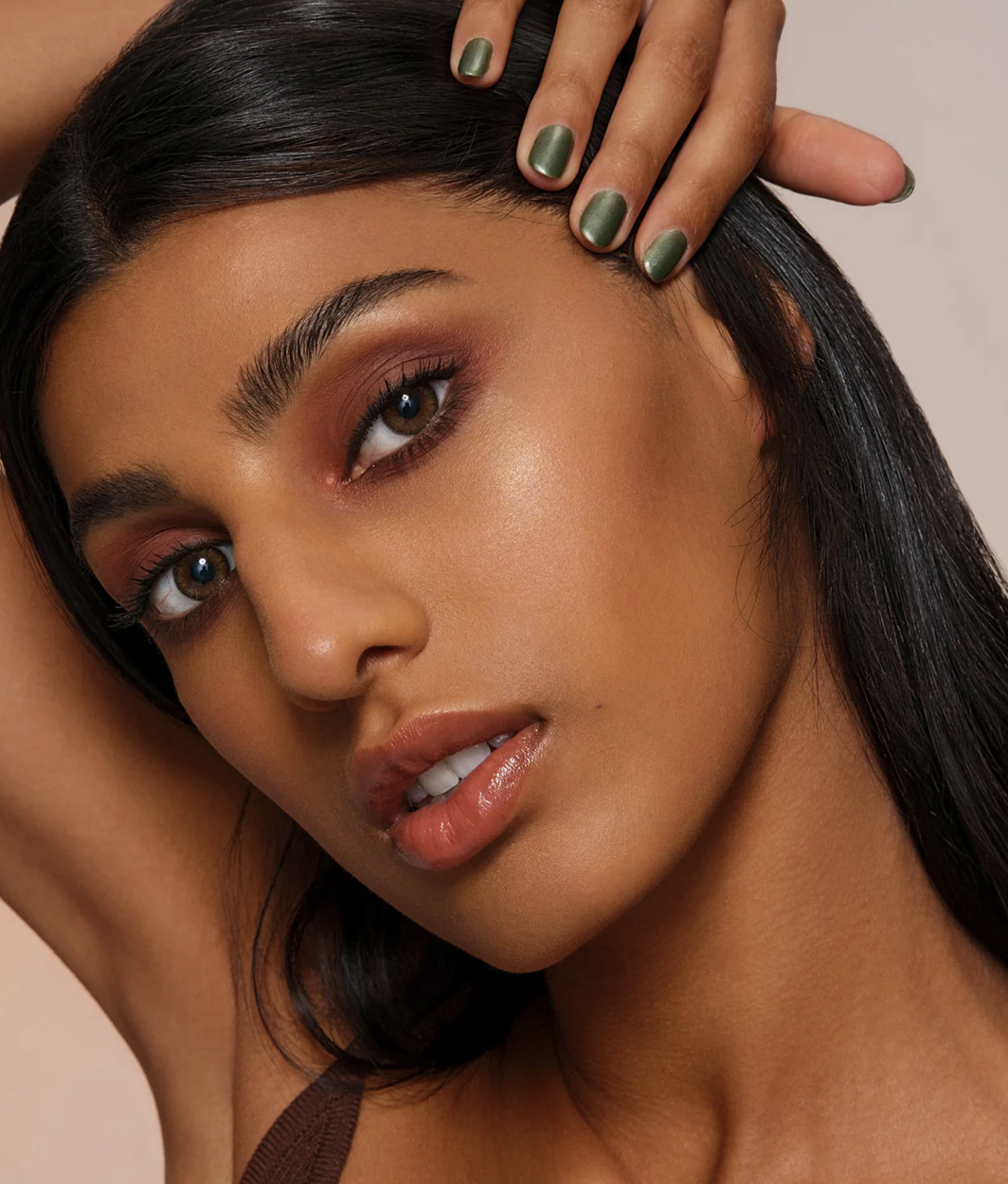 Close-up of a model wearing warm-toned eyeshadow and glowing skin with green nail polish, showcasing a natural, polished makeup look.