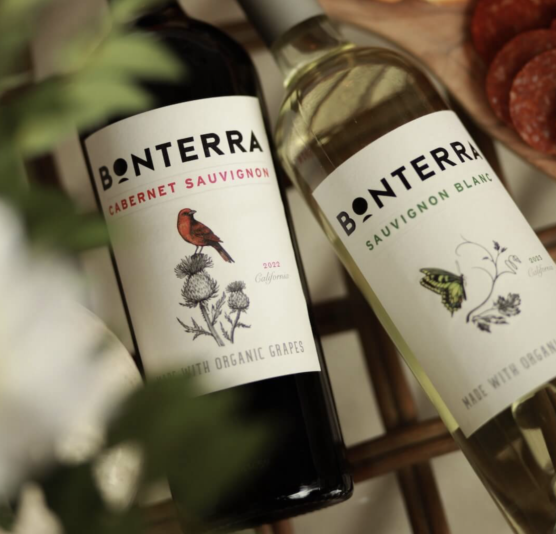 Two bottles of Bonterra Organic Estates wine on a wooden rack, featuring Cabernet Sauvignon and Sauvignon Blanc with illustrated labels.