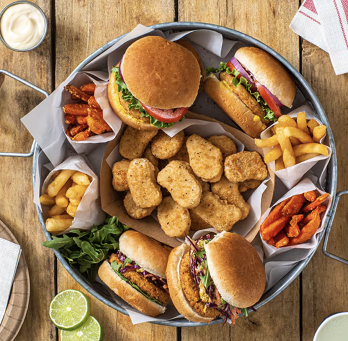 Overhead view of a tray filled with Quorn meat-free foods, including burgers, breaded nuggets and sandwiches, surrounded by fries, sweet potato fries and dipping sauces on a wooden table.