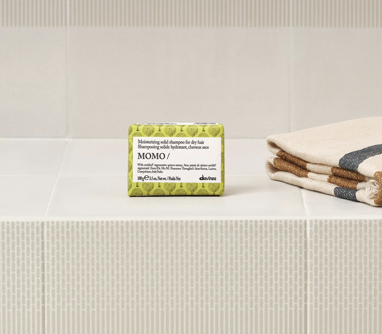 Davines MOMO solid shampoo bar displayed on a tiled bathroom shelf beside folded towels