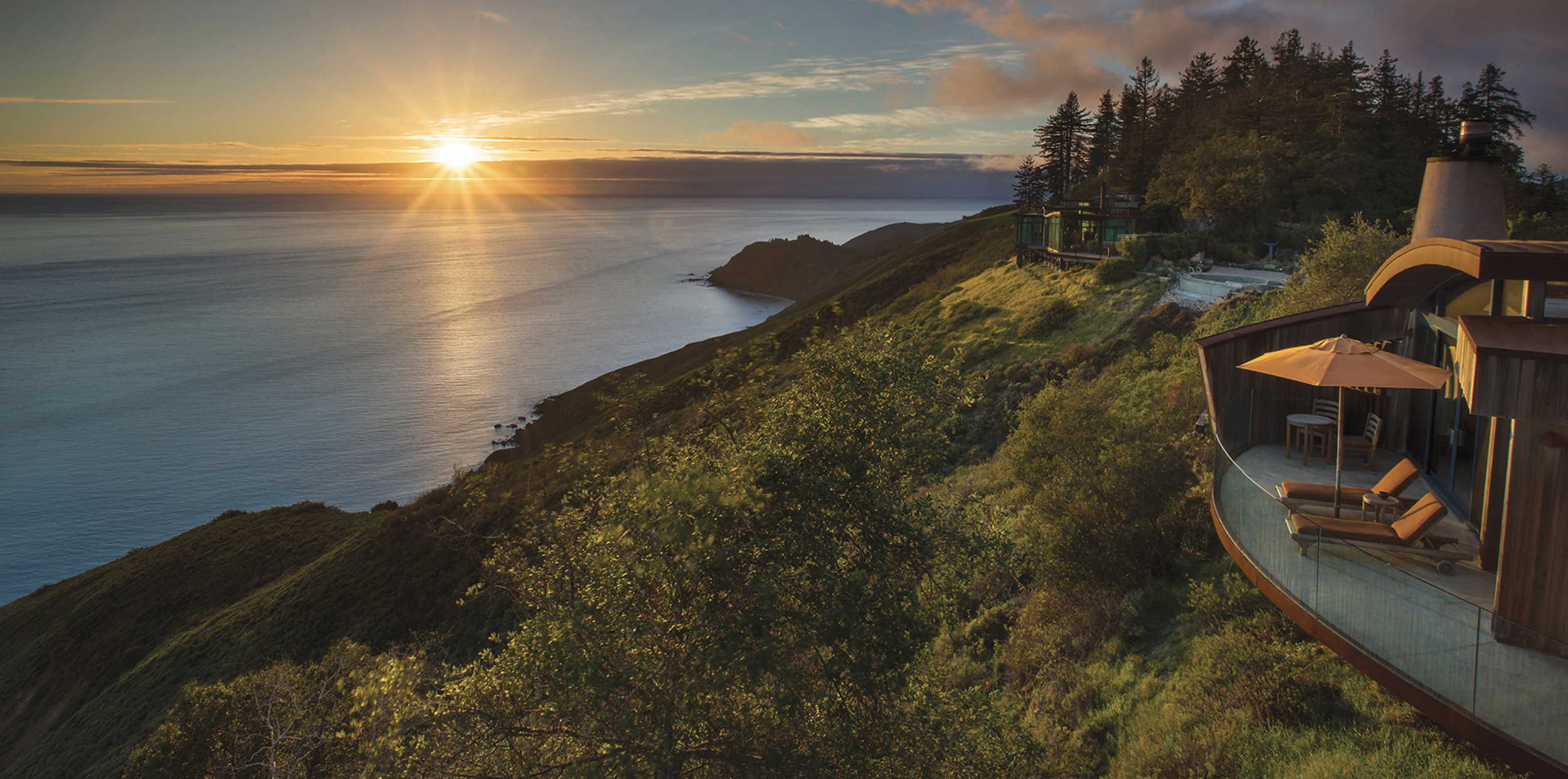 Cliffside eco-lodge with curved balconies at Post Ranch Inn in Big Sur overlooking the Pacific Ocean at sunset.