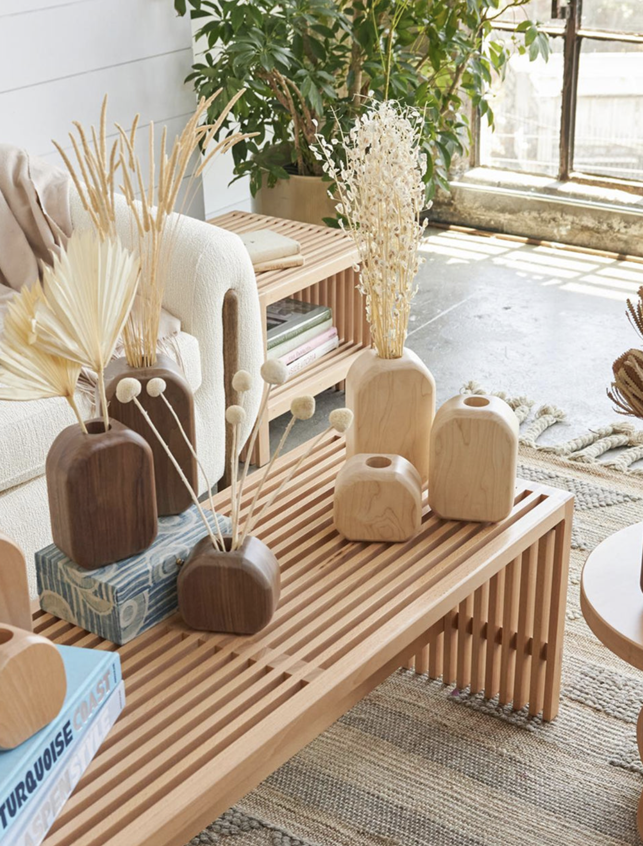 Avocado wood coffee table and decor with natural wood vases, dried botanicals and neutral textiles in a bright, plant-filled living space