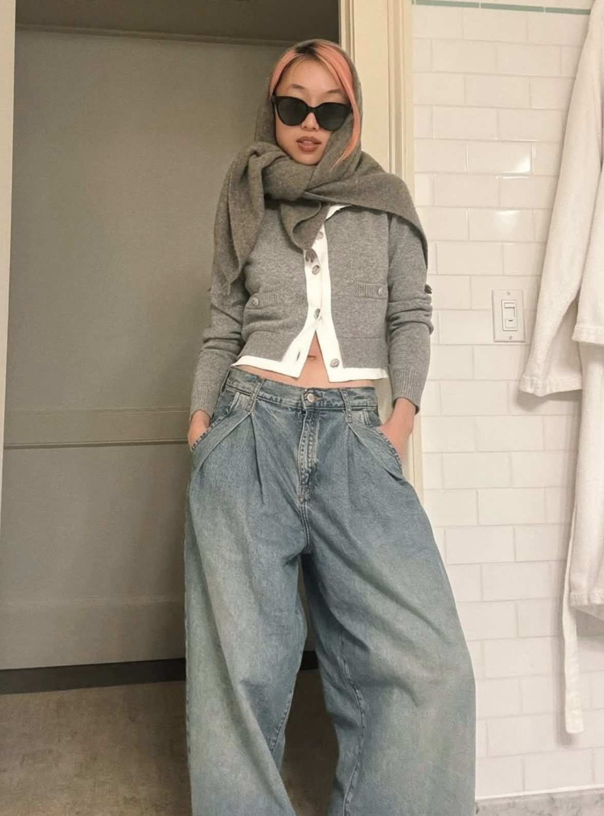 Woman wearing relaxed, wide-leg Triarchy jeans styled with a cropped cardigan, scarf and sunglasses, standing in a casual indoor setting