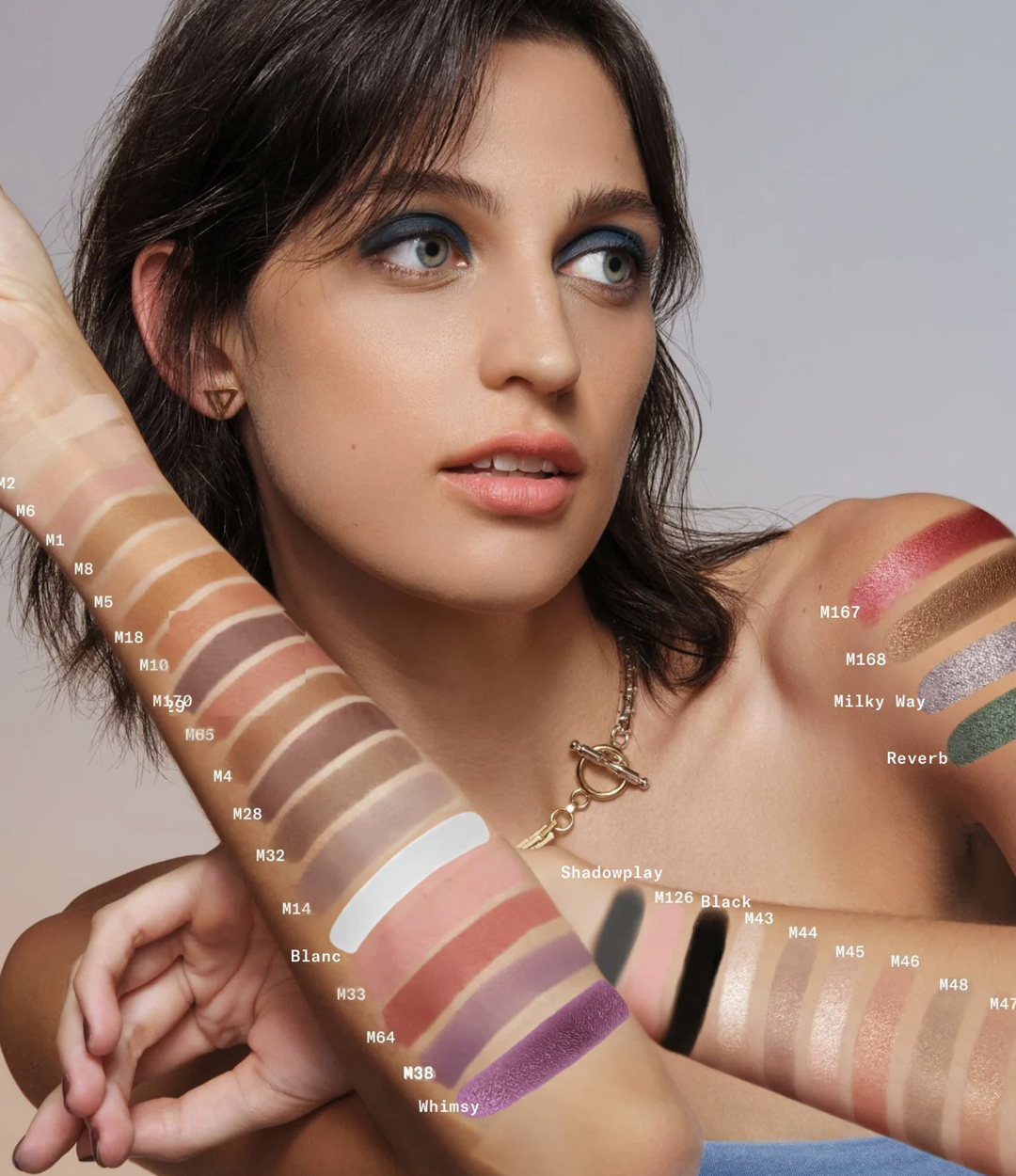 Model with swatches of foundation and eyeshadow shades displayed along her arm and shoulder, highlighting a wide range of tones and colors.