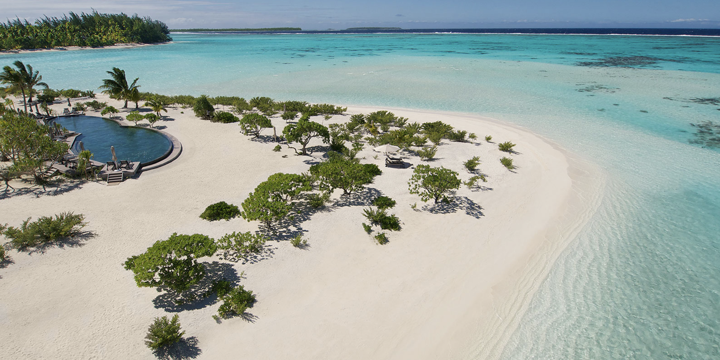 Aerial view of a pristine white sand island at The Brando in French Polynesia surrounded by clear blue water and a lagoon pool.