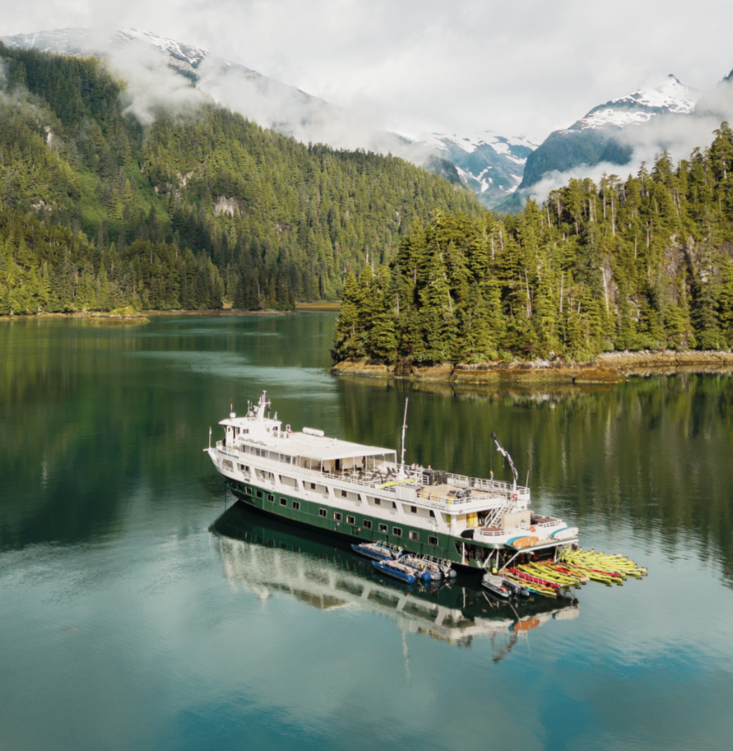 UnCruise Adventures small ship navigating a forested fjord surrounded by mountains in Alaska
