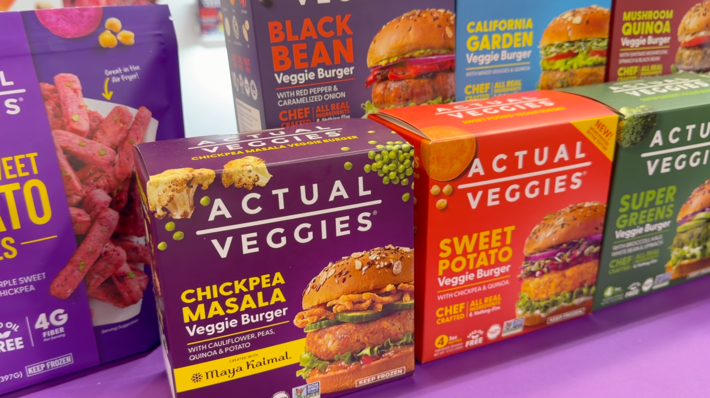 Full Actual Veggies product lineup including Chickpea Masala, Sweet Potato, Black Bean, California Garden, Mushroom Quinoa and Super Greens Veggie Burgers alongside Purple Sweet Potato Super Fries, displayed in their colorful packaging.