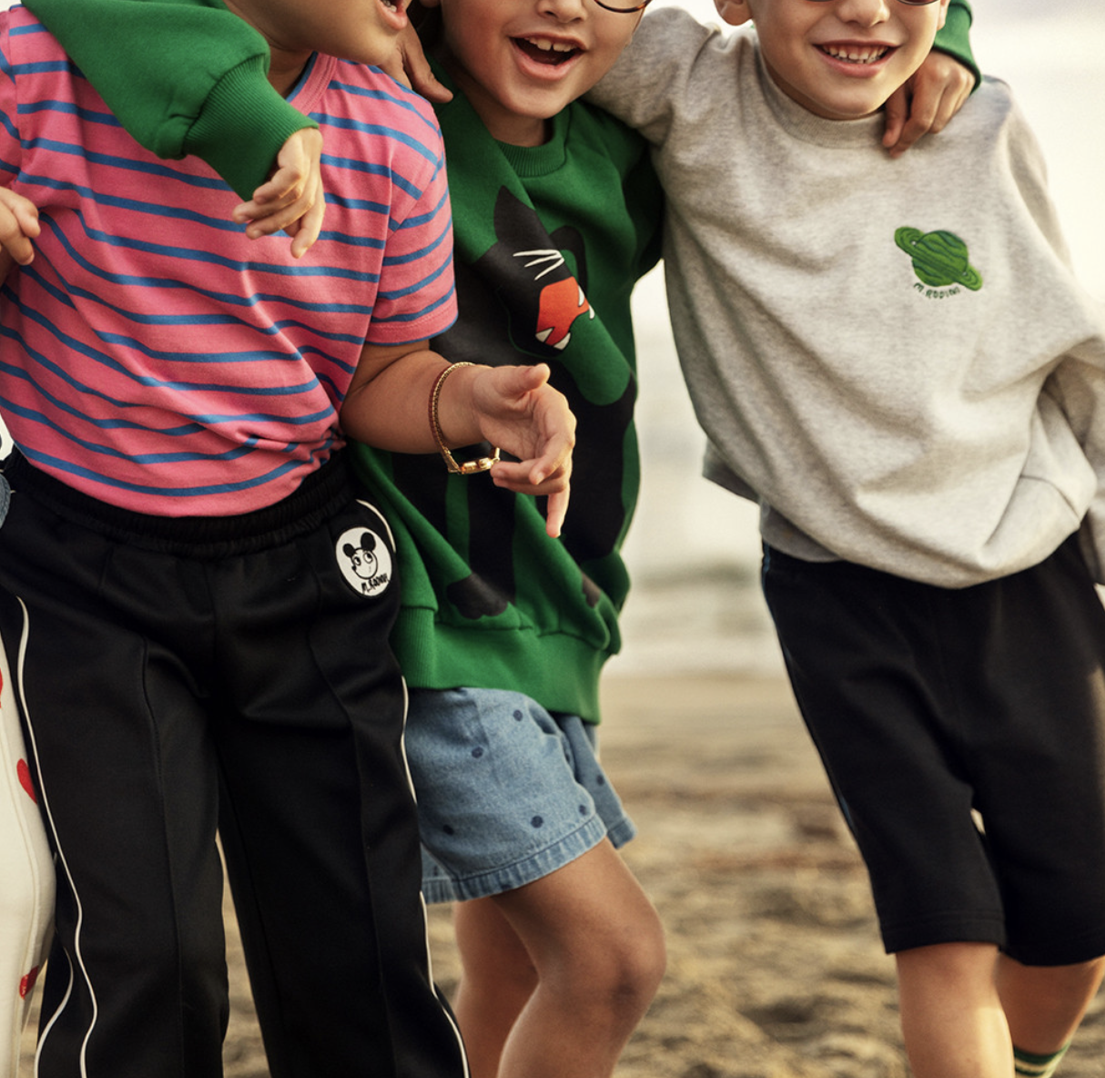 Children wearing colorful Mini Rodini outfits including striped shirts, graphic sweatshirts and sporty shorts while walking together outdoors