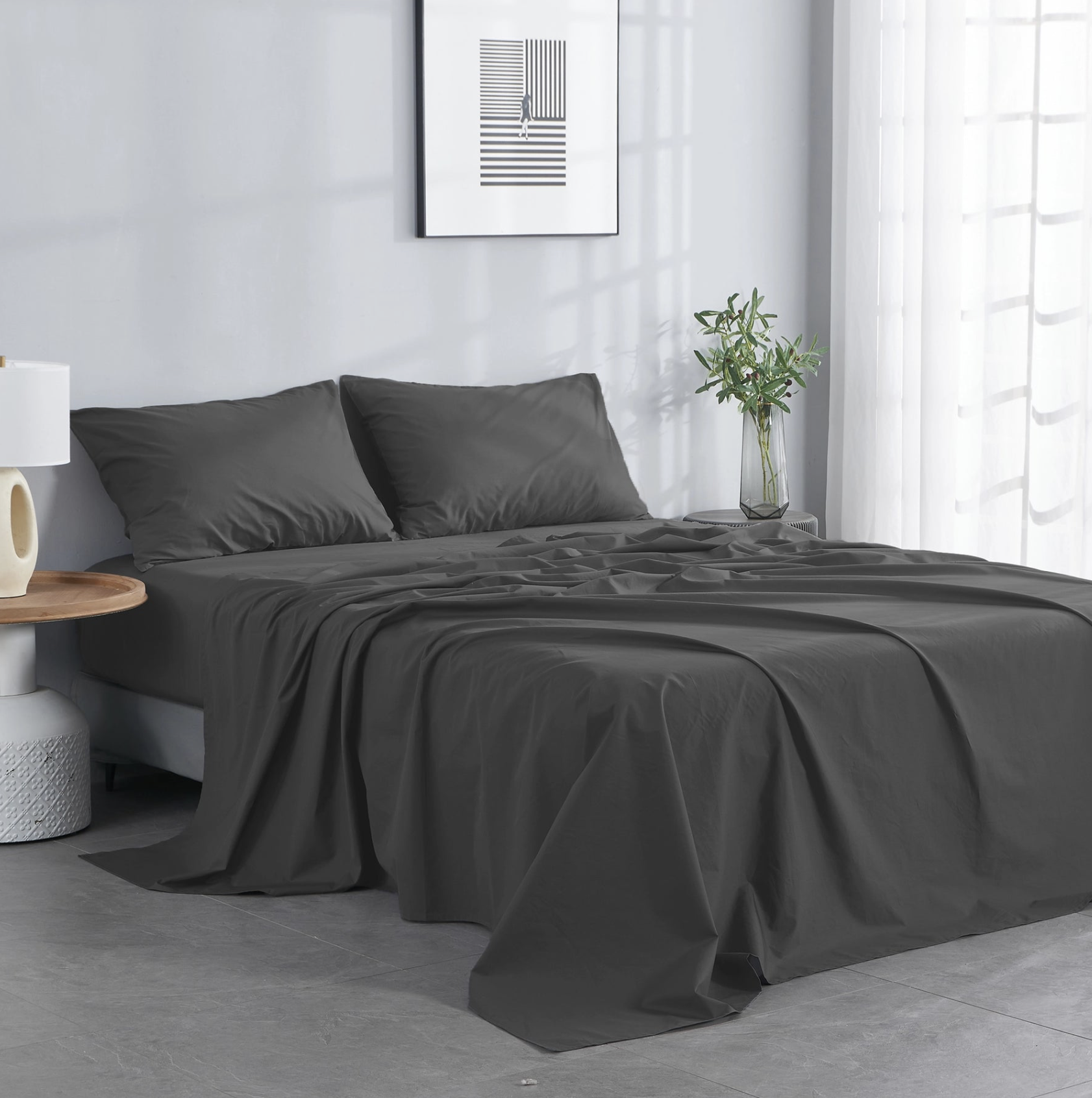 Bed with dark gray sheets and pillows in a modern bedroom with light walls and minimal styling.