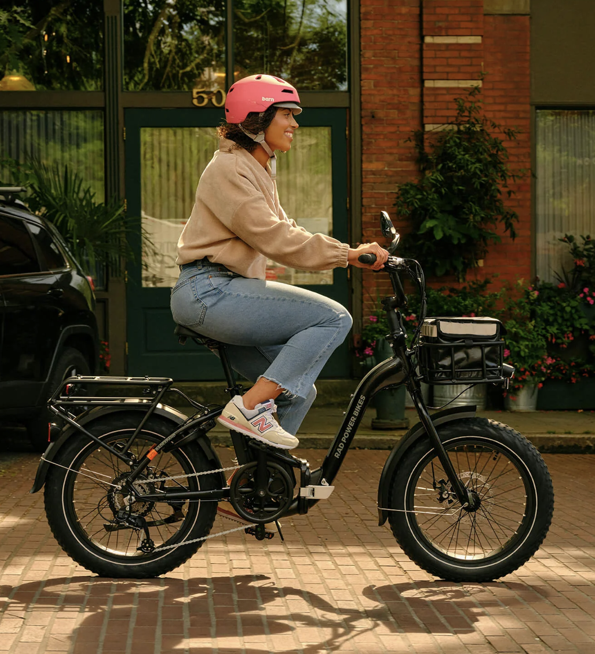 A woman wearing a pink helmet rides a Rad Power Bikes electric bike through a city street, showing a compact e-bike designed for everyday urban transportation.
