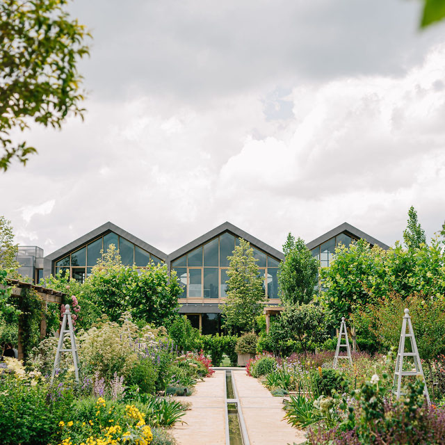 Modern greenhouse-style buildings surrounded by lush gardens and landscaping at the Davines Village headquarters in Parma, Italy