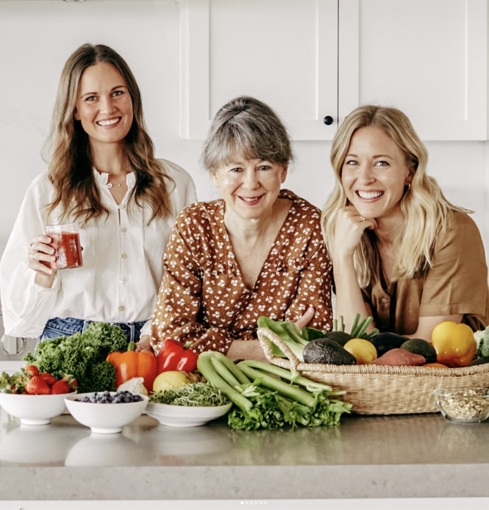Three Branch Basics co-founders smiling in a bright kitchen, gathered around fresh fruits and vegetables, reflecting the brand’s focus on health, wellness and toxin-free living