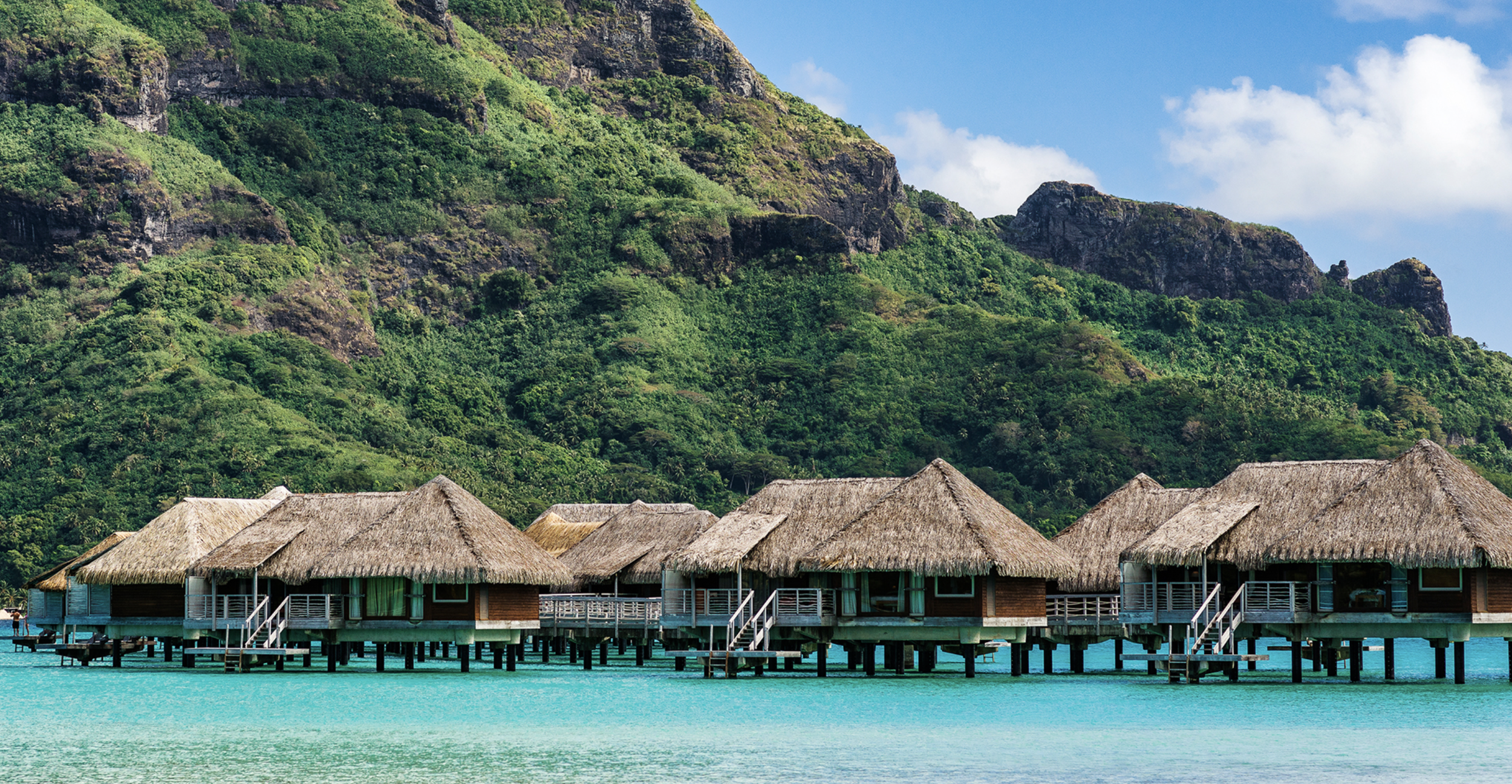 Overwater bungalows at InterContinental Bora Bora set above turquoise lagoon waters with lush green mountains rising in the background.
