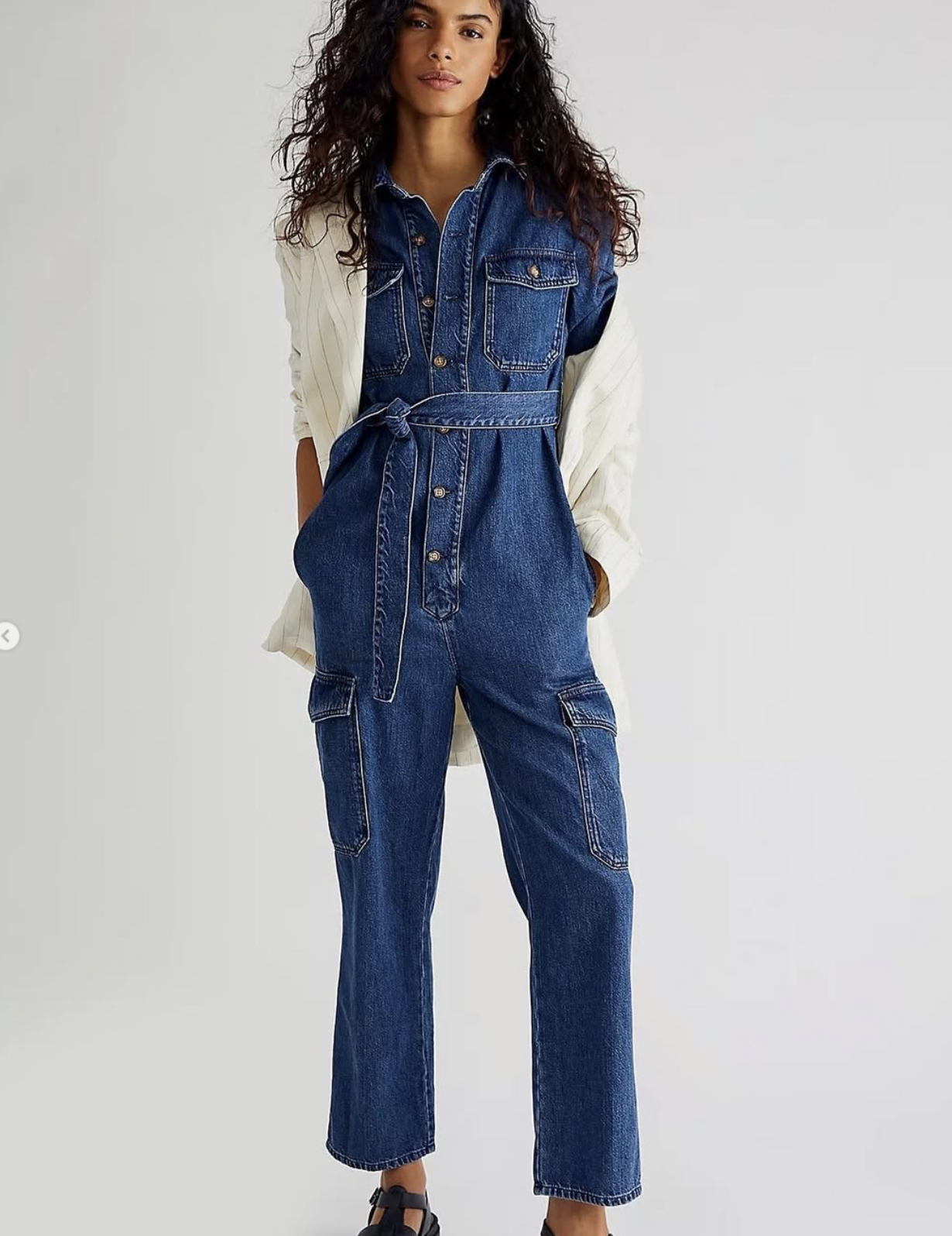 Woman wearing a denim jumpsuit by Boyish, styled with a belted waist and utility pockets, paired with sandals in a clean studio setting