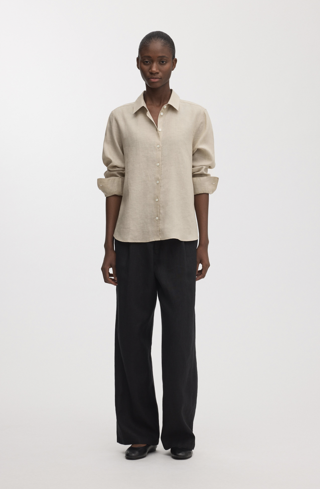 Model wearing a beige button-down shirt with black wide leg trousers and black flats against a neutral background.