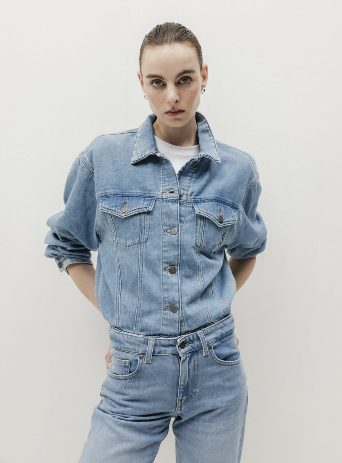 Woman wearing a light wash denim jacket and matching jeans set, styled in a clean studio setting with a minimal background