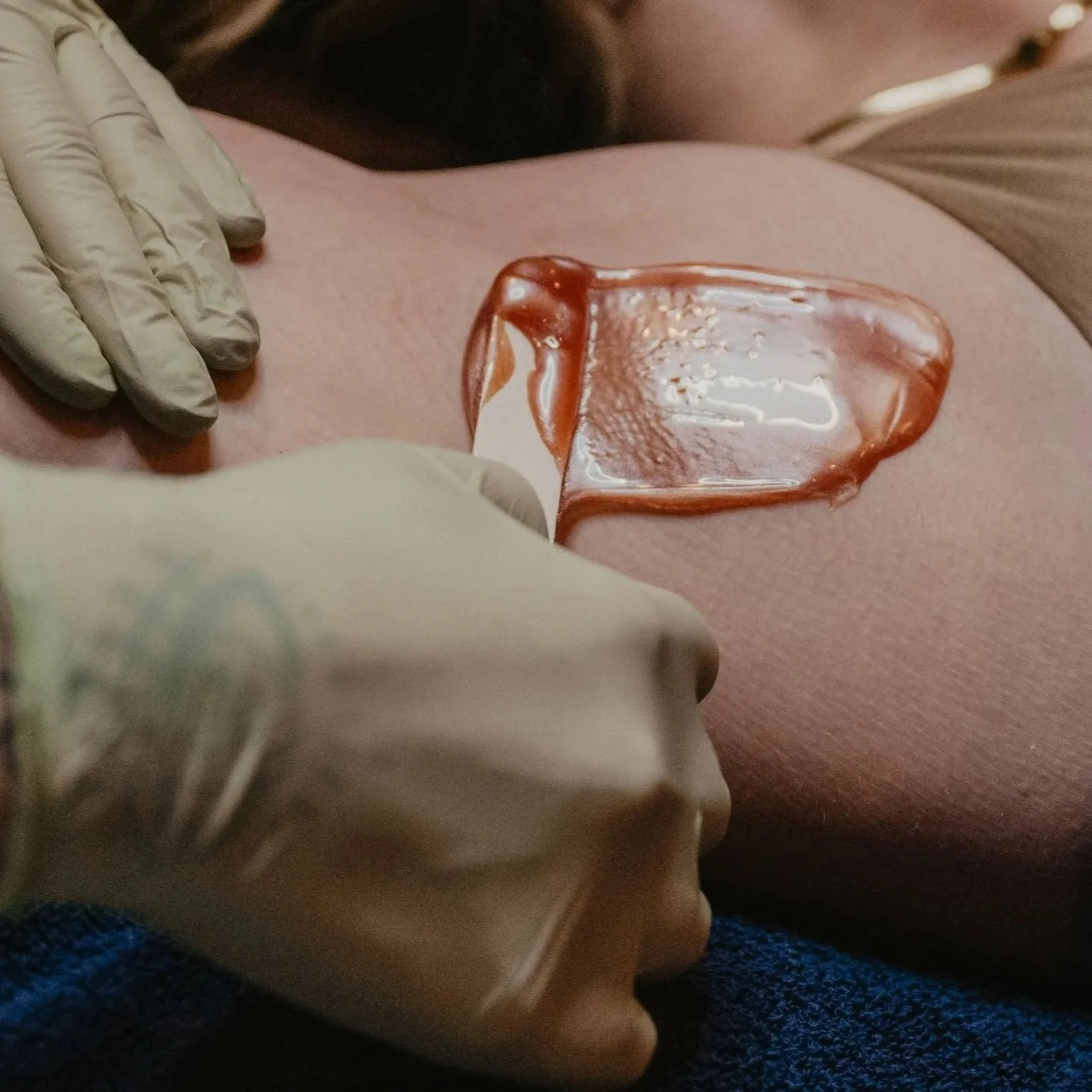 Close-up of a person applying wax on skin with gloves and spatula