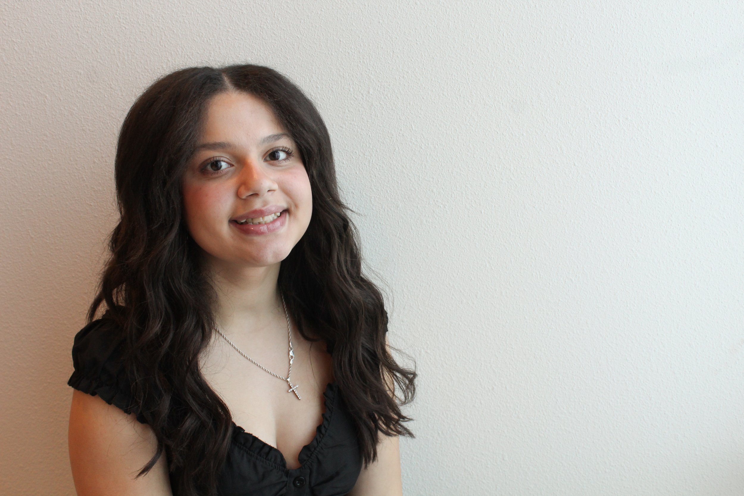 Smiling woman with wavy hair wearing a knitted sweater against a light background.