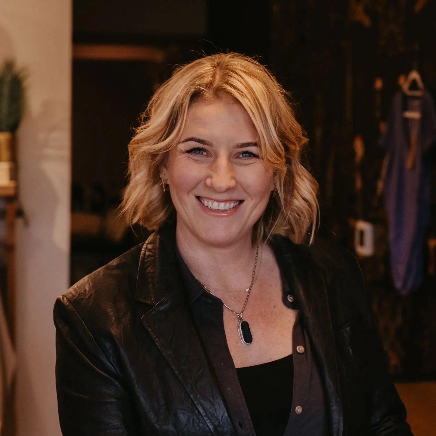 Smiling woman with blonde hair at reception desk in a modern, stylish store or cafe.