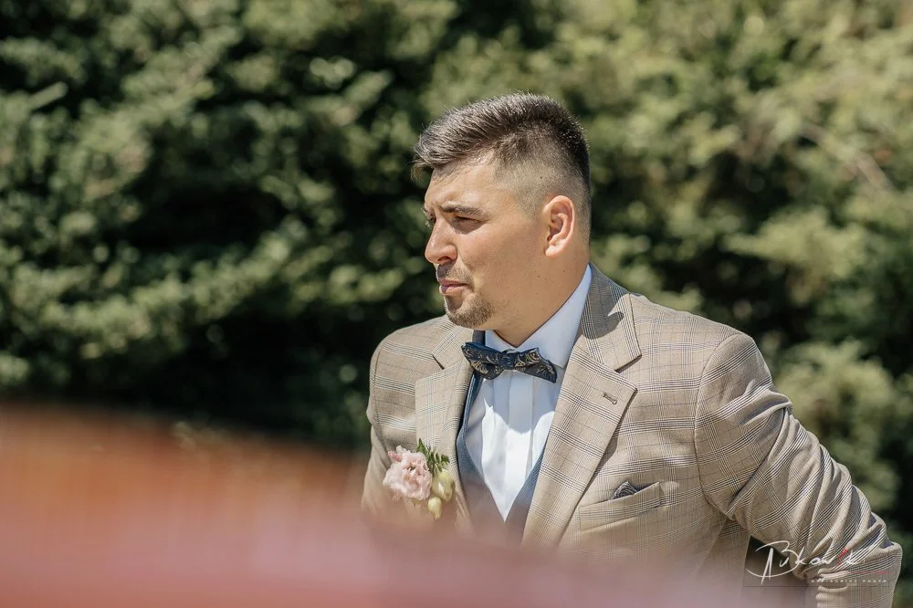 A man in a plaid suit with a bow tie and boutonniere outdoors.
