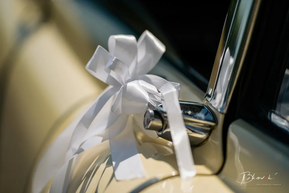 Close-up of a car door handle with a white ribbon tied in a bow, suggesting a wedding or celebration event.