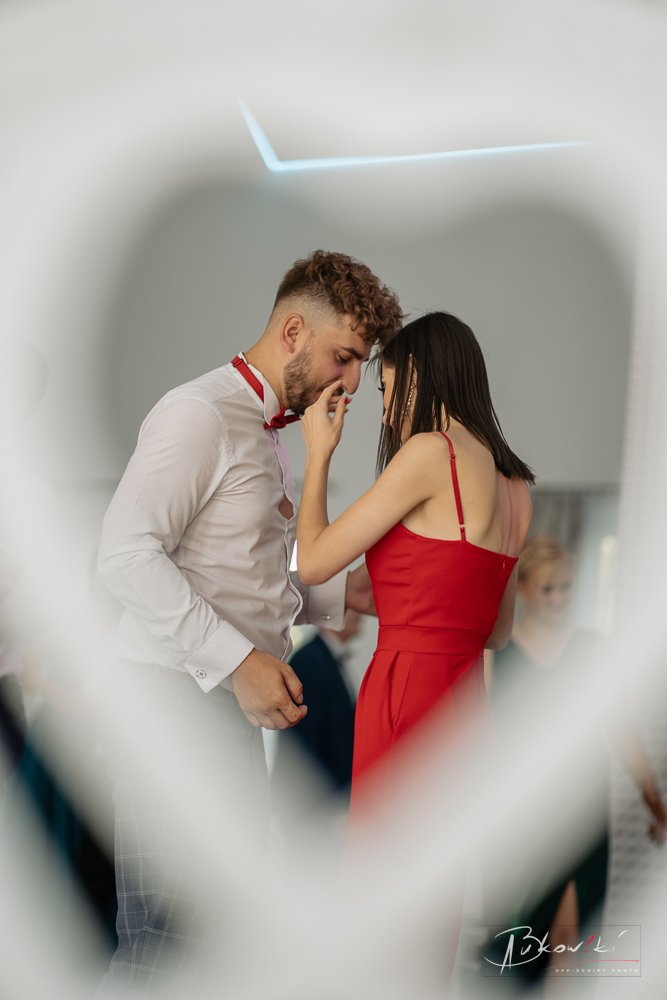 A young man and woman sharing an intimate moment, touching foreheads and holding hands, seen through a blurred white design element.