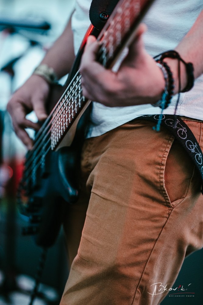 Close-up of a person playing an electric guitar, wearing brown pants, a white shirt, and bracelets on their wrist.
