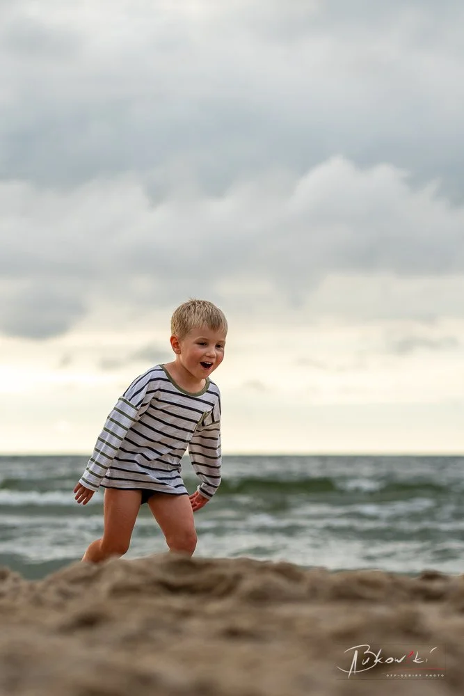 A young boy running on the beach near the ocean on a cloudy day.