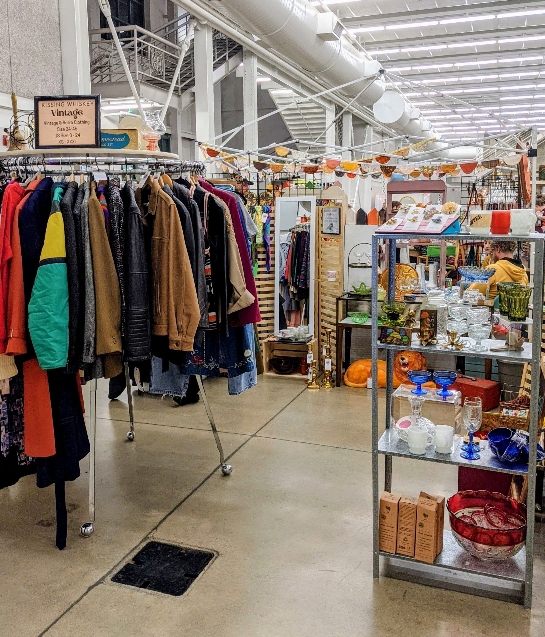 Inside a thrift store with clothing racks and shelves displaying glassware and decorative items.