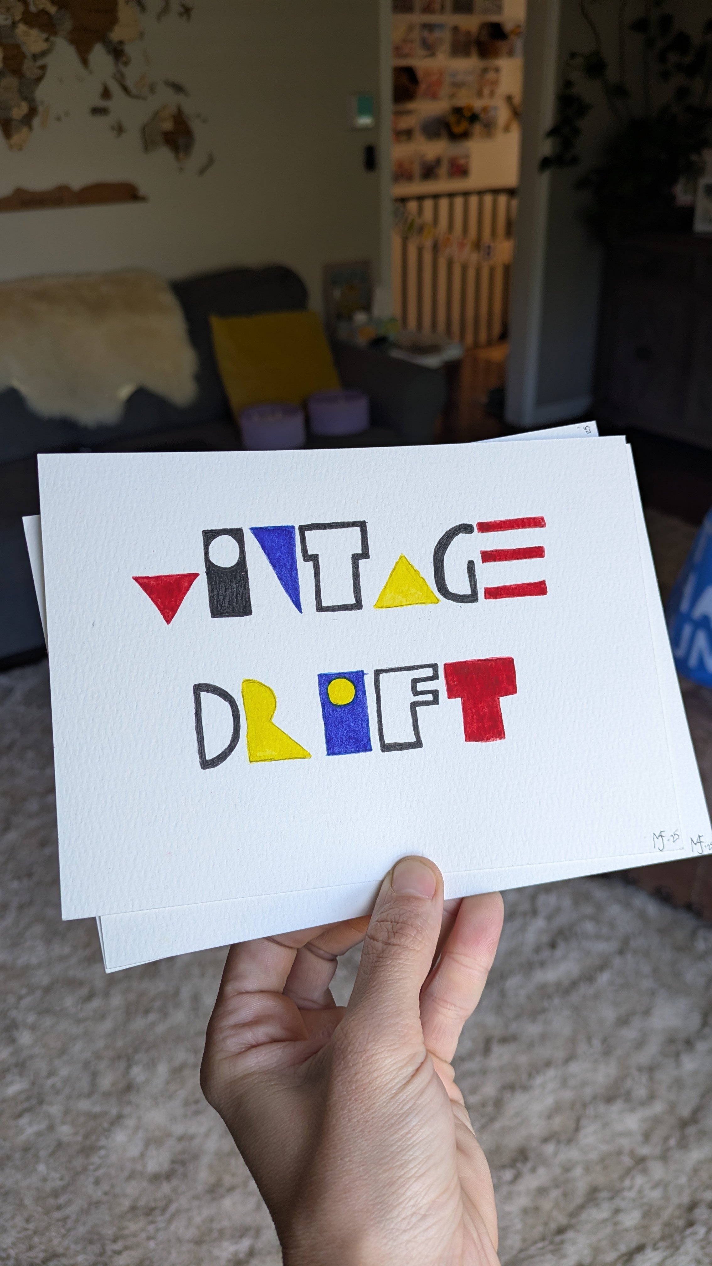 A white card with the words "VINTAGE DRAFT" written in colorful, playful letters, being held by a person's hand in a home living room.